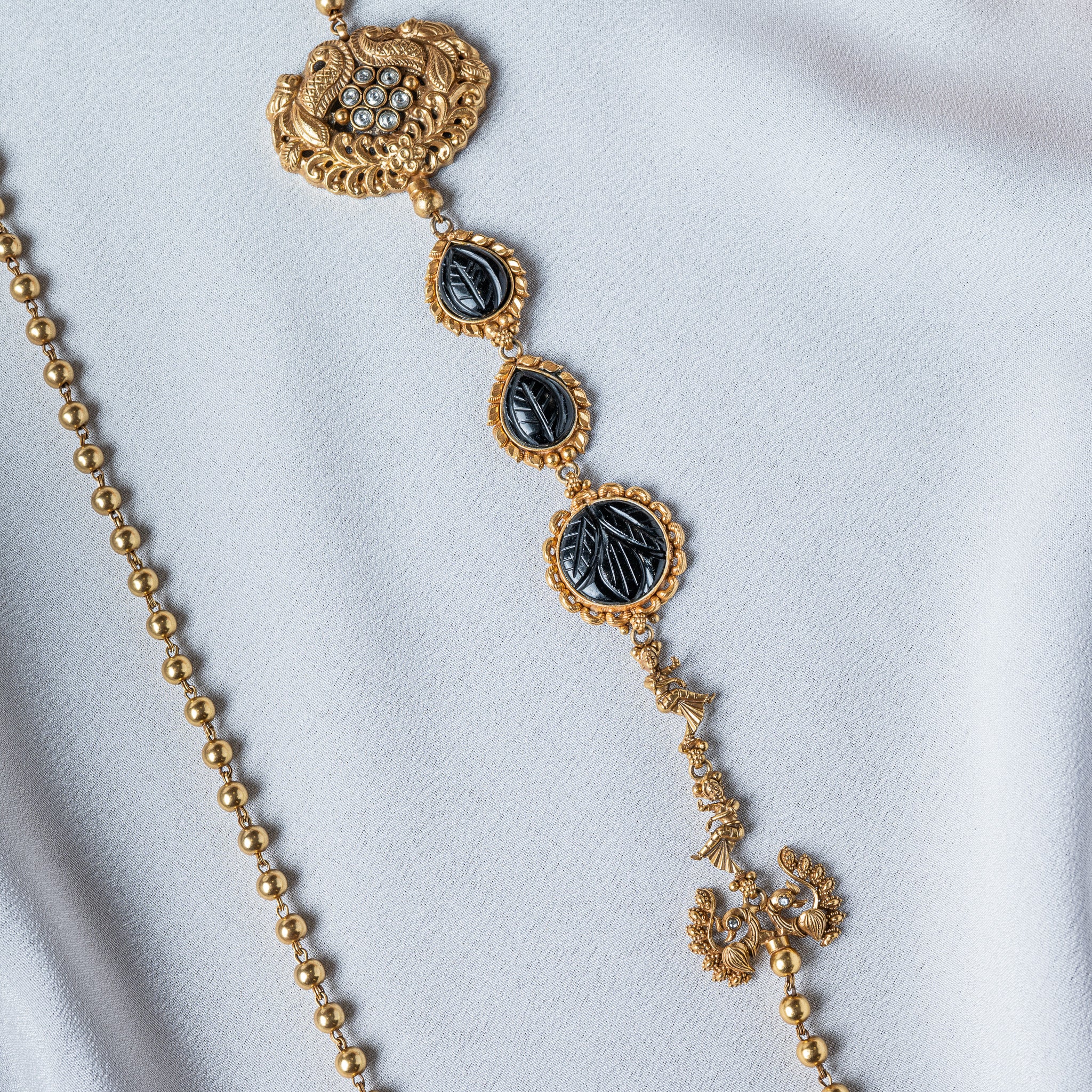 Raised peacock medallion with its tail scrolling around seven white kundan, close crop