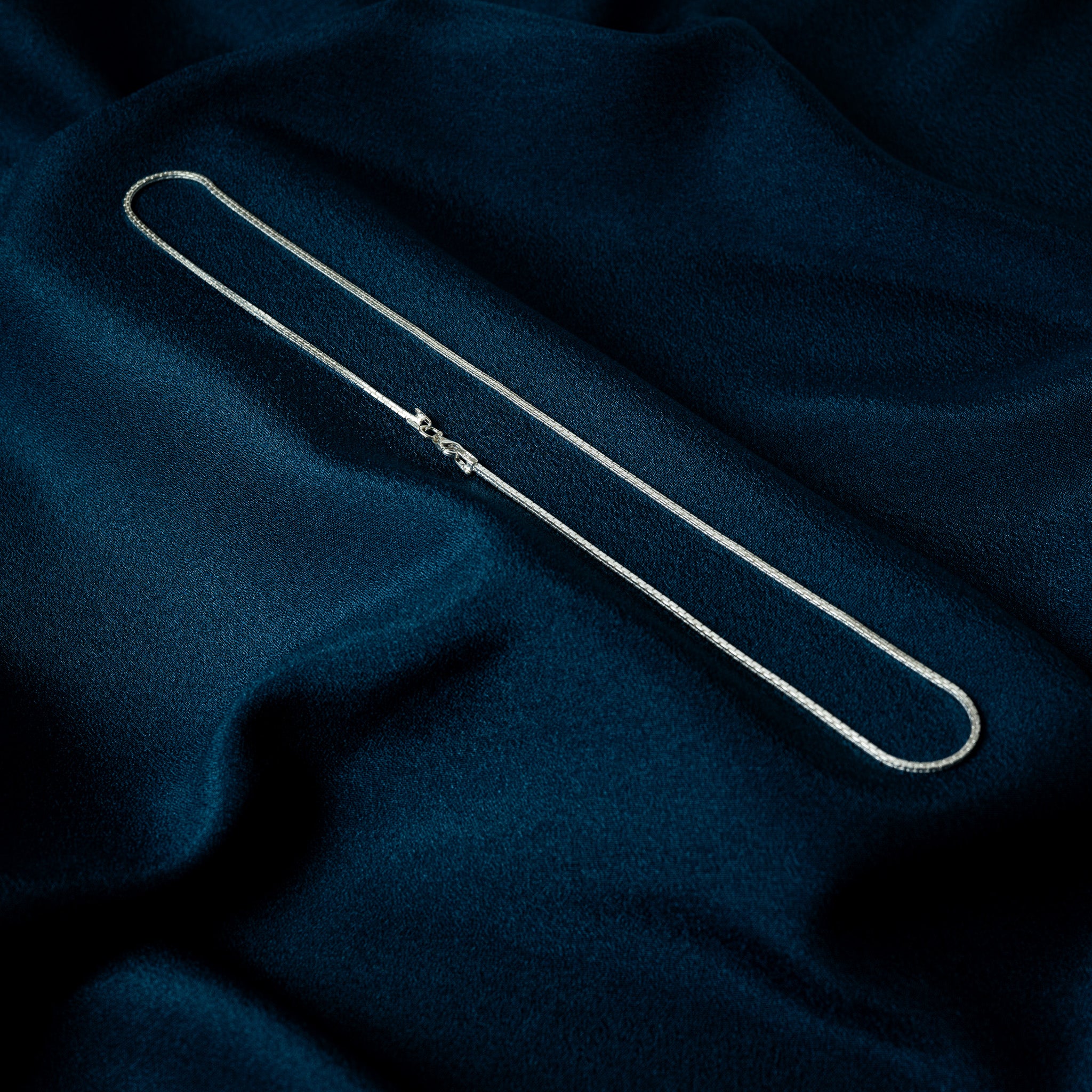Side view of a silver faceted box chain showing its squared profile