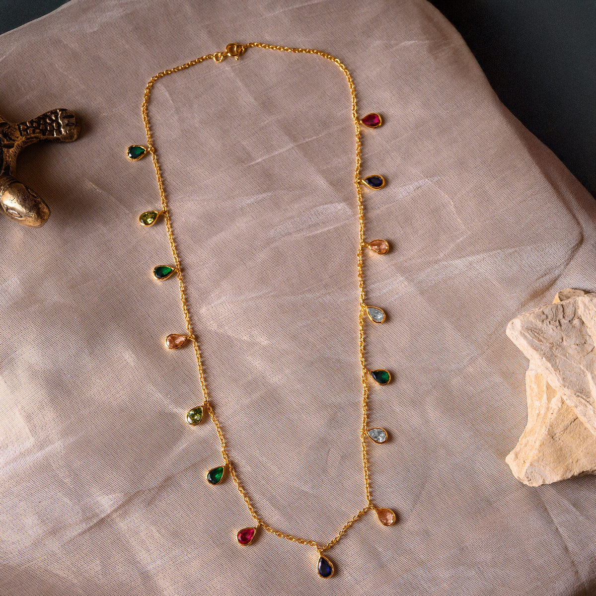 Close view of pear multicolour stones set into gold rims along the fine chain of the necklace
