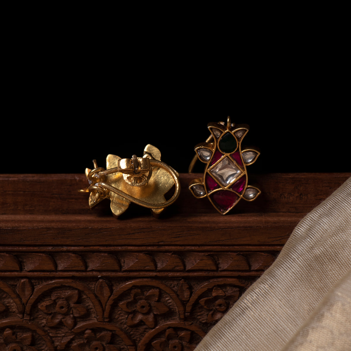 Green pear stone at the top of the lotus bud stud, angled view over pink red and white kundan