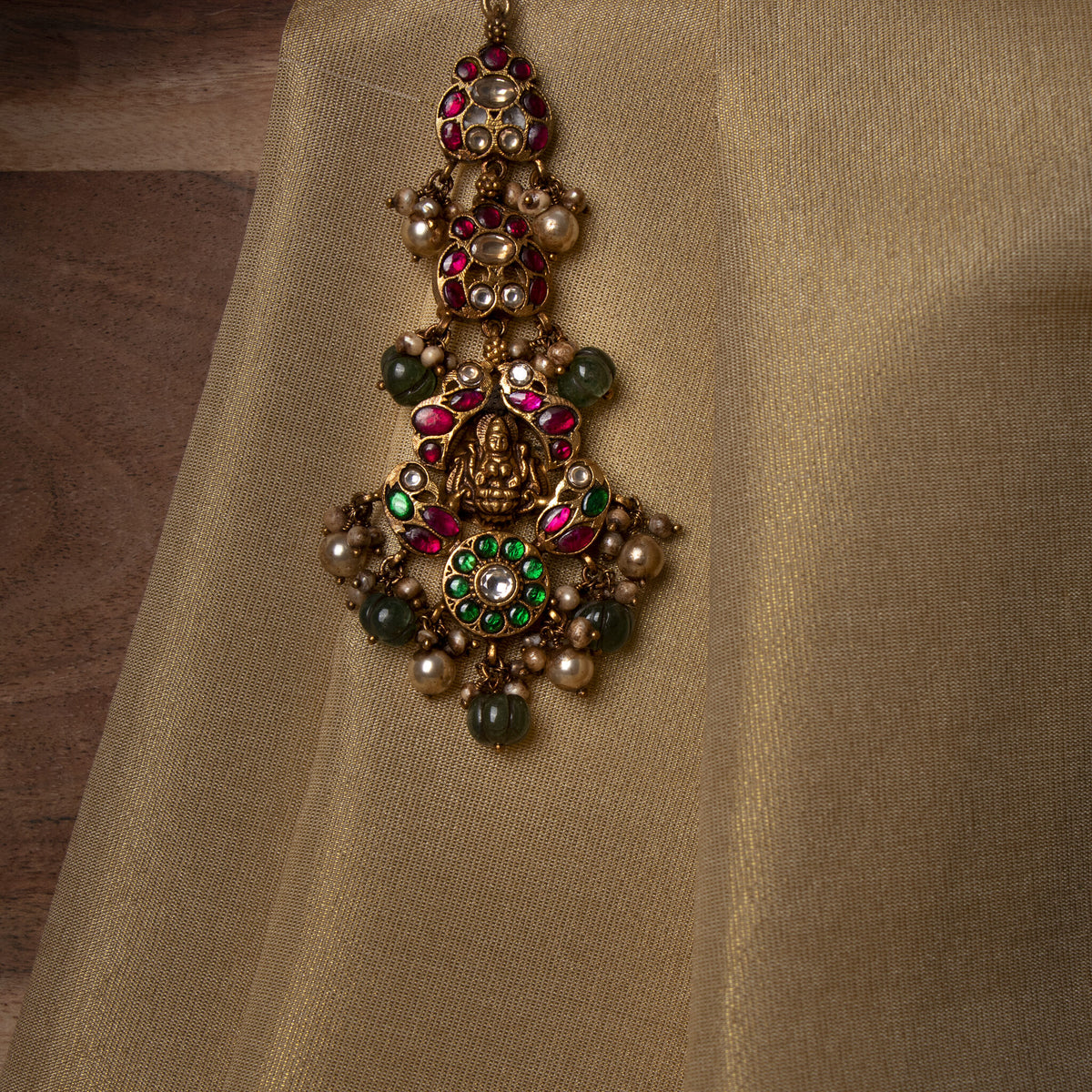 Green kundan flower disc and carved green bead ending the maangtika drop below the Lakshmi centre
