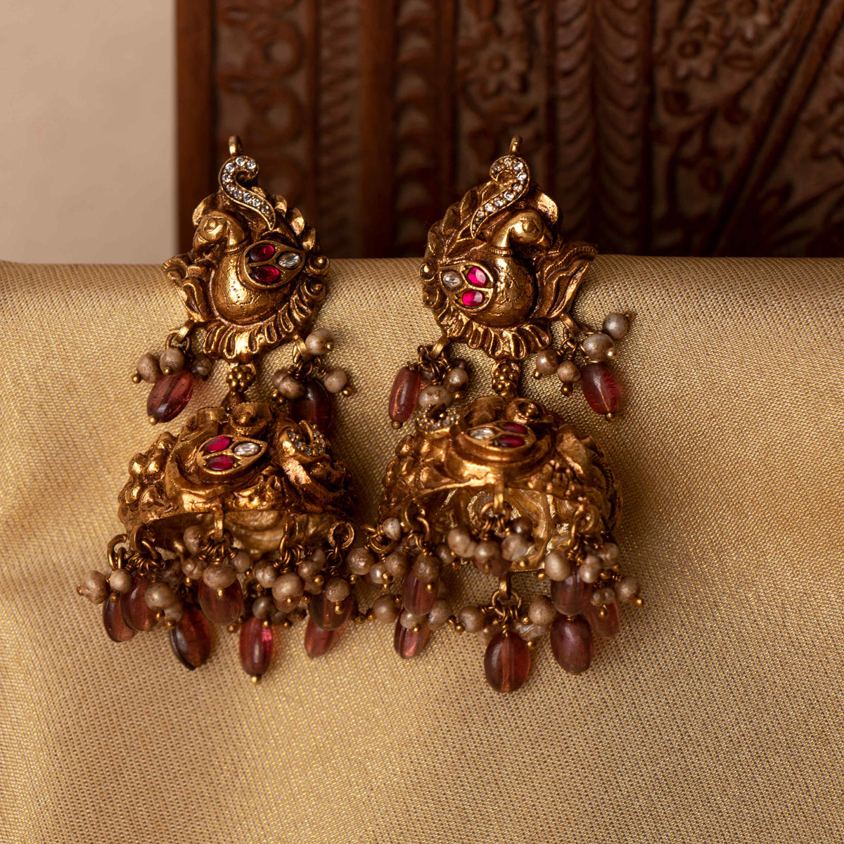 Nakaashi peacock jhumkas with carved dome, maroon bead and grey pearl drops, antique gold plated silver.