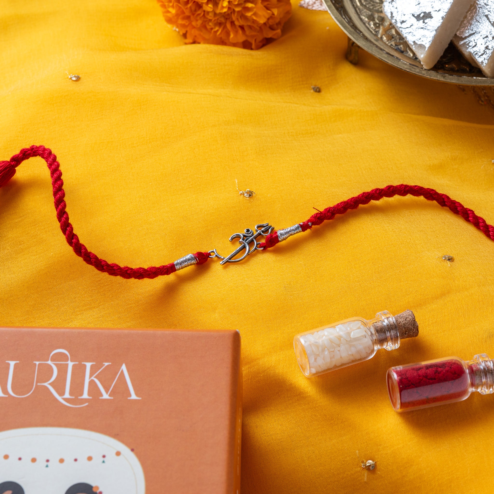 Om trishul rakhi in 925 silver on a marigold yellow silk cord, on rani pink cloth