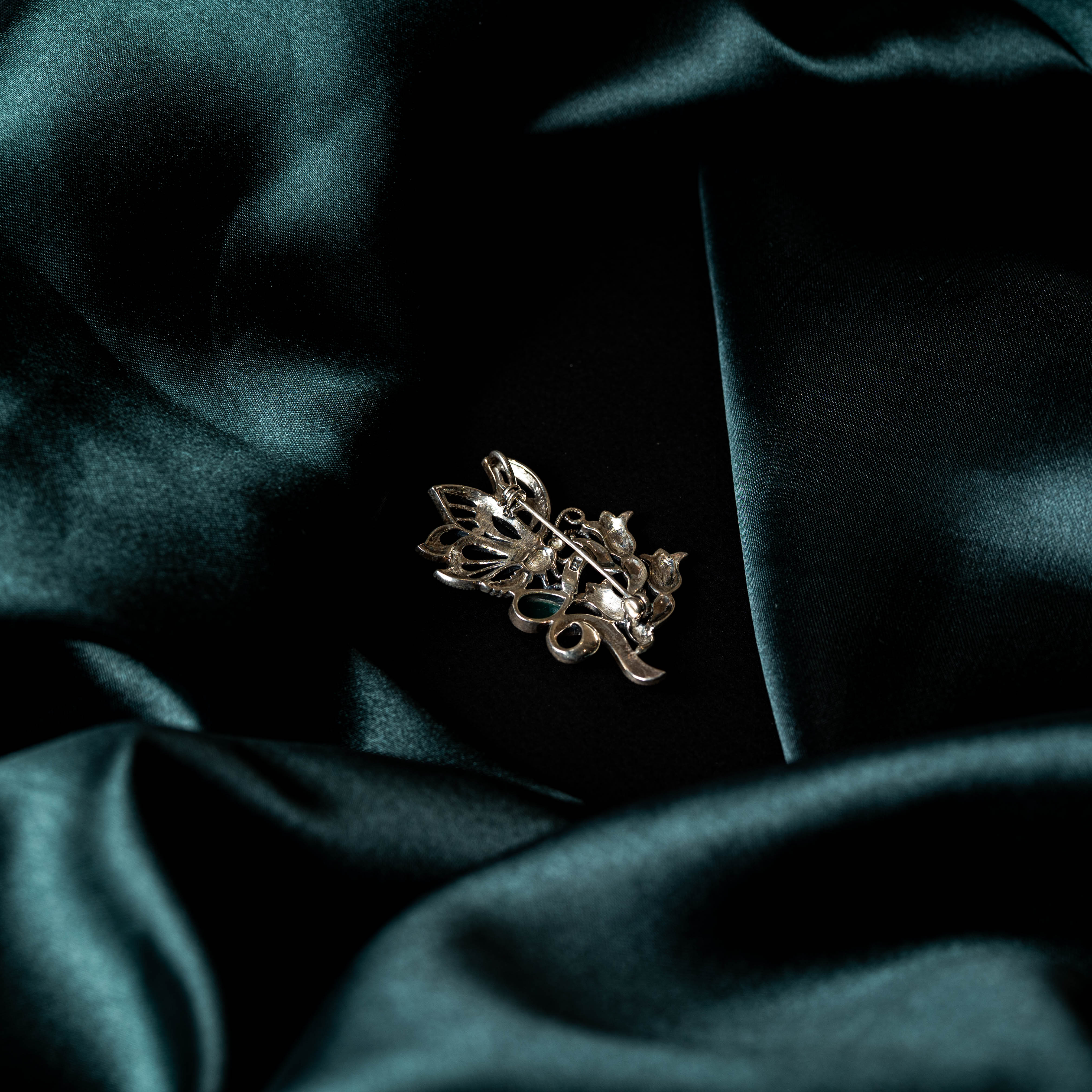 Floral scroll brooch with marcasite detailing and a green stone accent in oxidised 925 silver