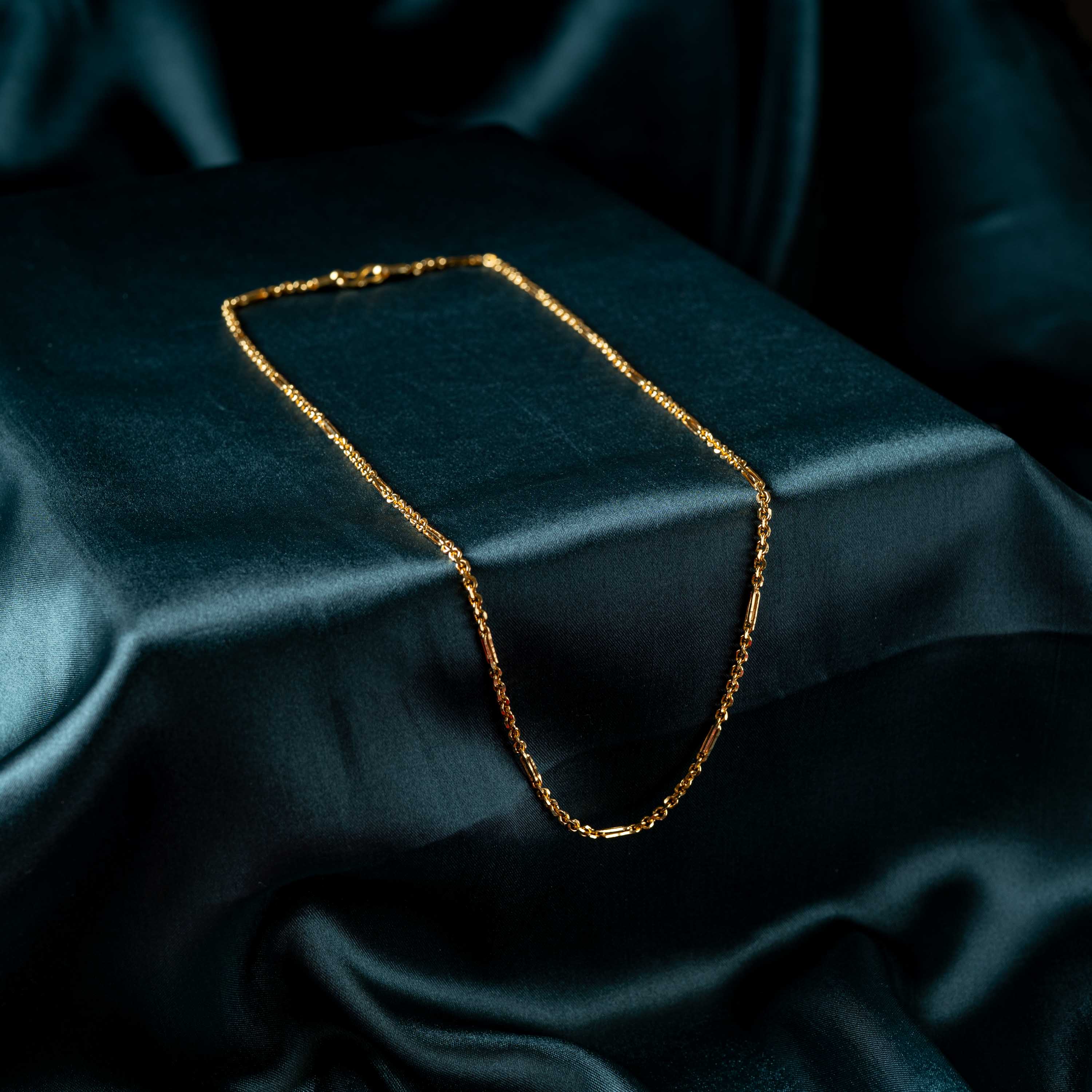 Chain draped in a curve over satin, alternating bar and cable links in gold plated 925 silver