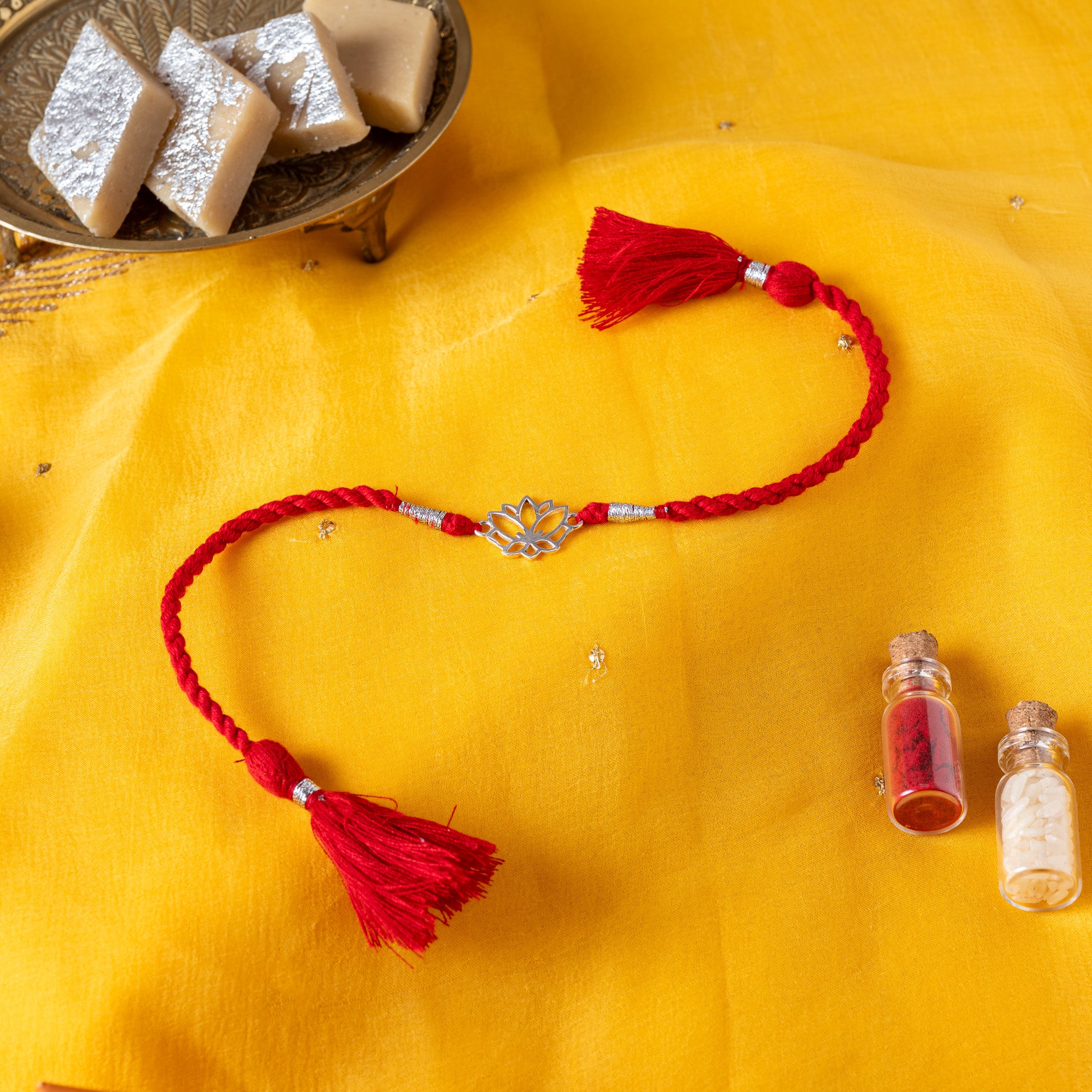 Lotus in profile with petals cut right through in 925 silver on a red twisted silk rakhi cord with tassels