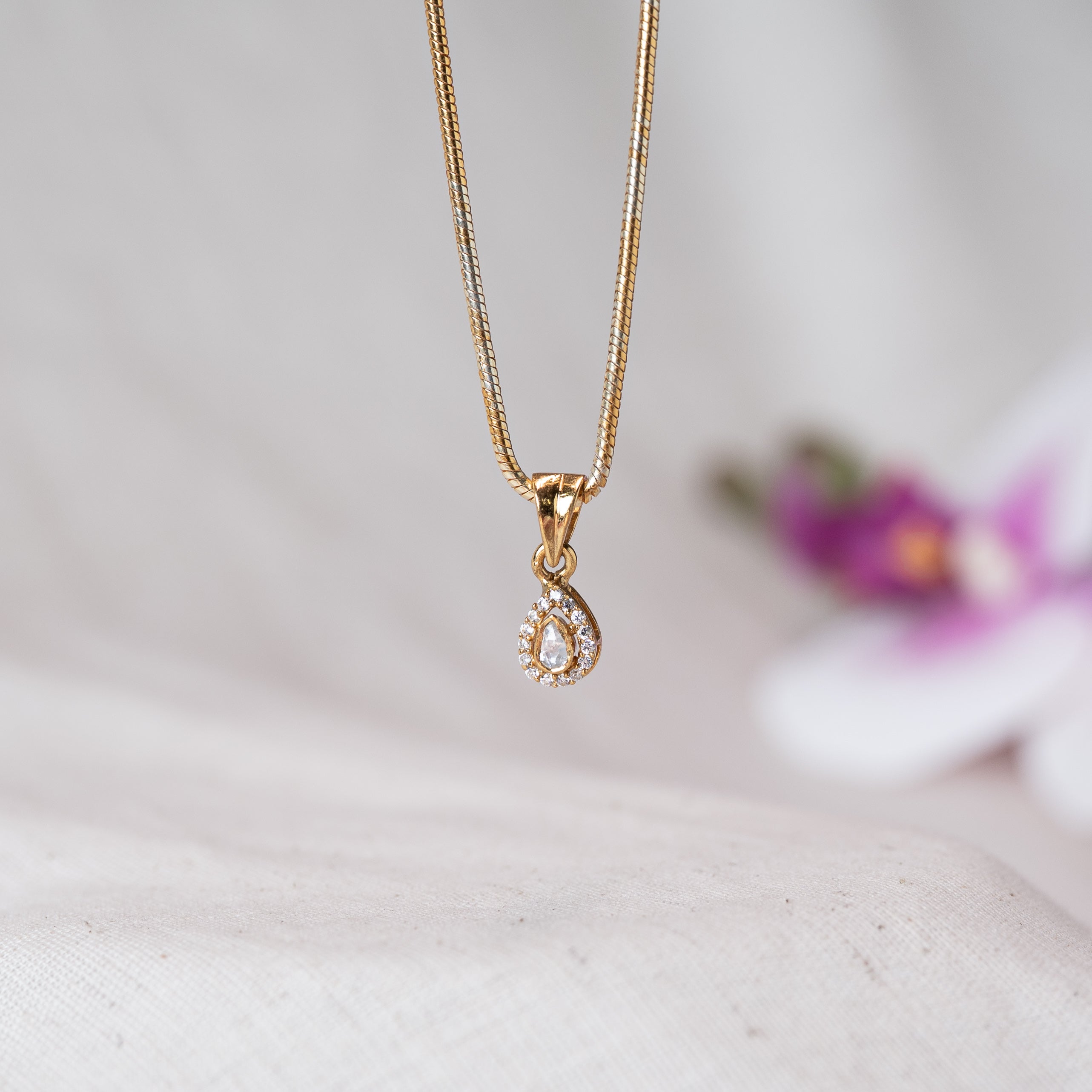 Close view of the polki teardrop pendant in its CZ halo hanging from the bail on a gold plated chain