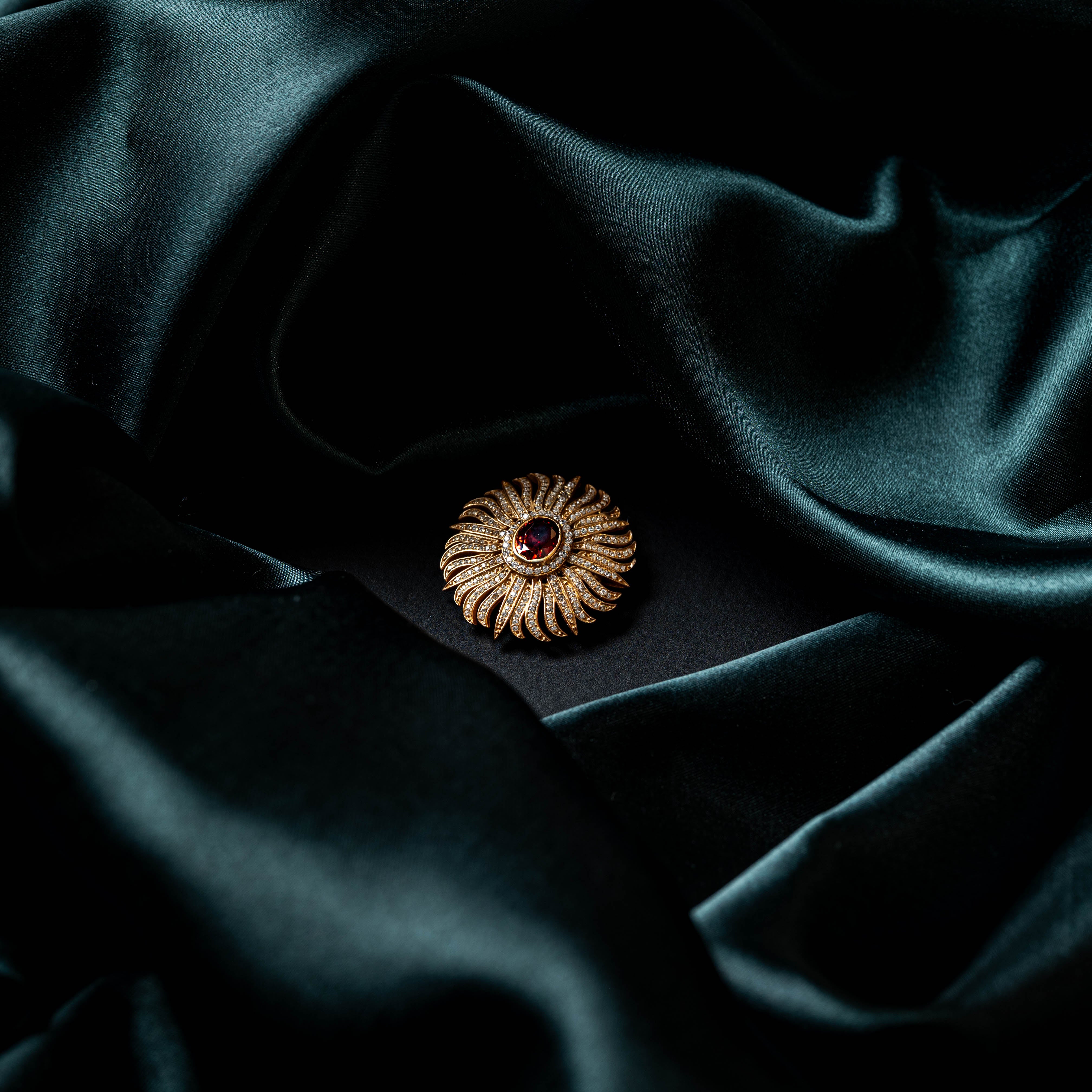 Sunburst brooch centred on dark satin, ruby centre ringed by CZ and fluted gold rays