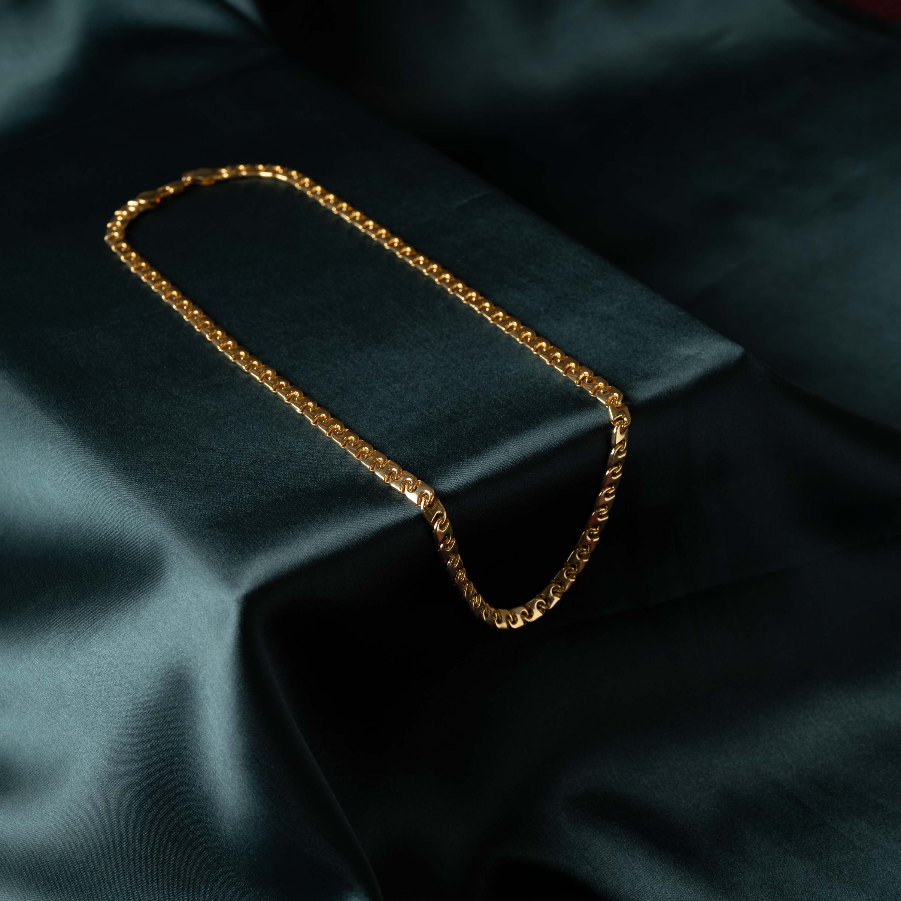 Full length of the scroll link chain laid in a loop on satin, gold plated 925 silver