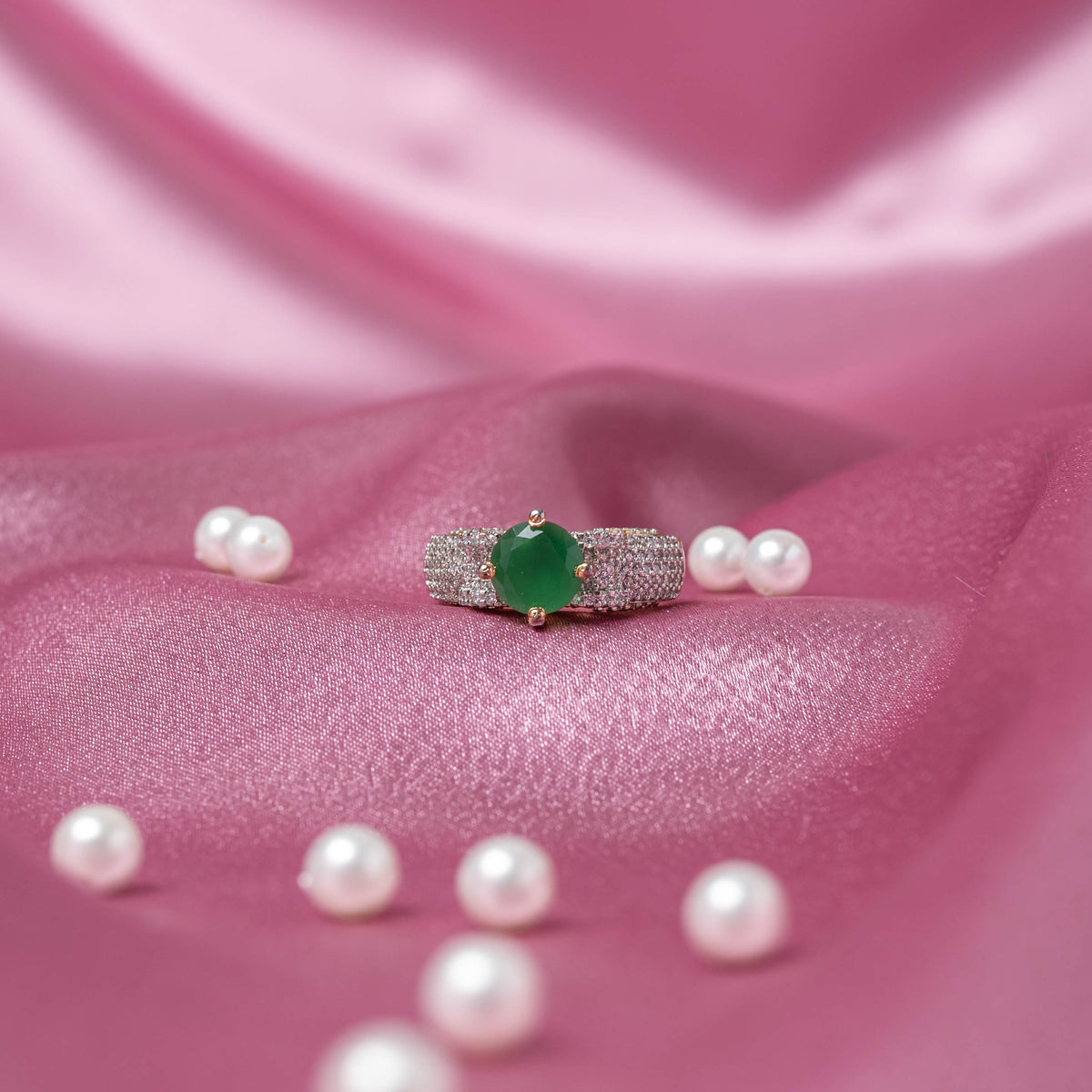 Angled view of the triple row CZ pave band below a round emerald-green centre stone