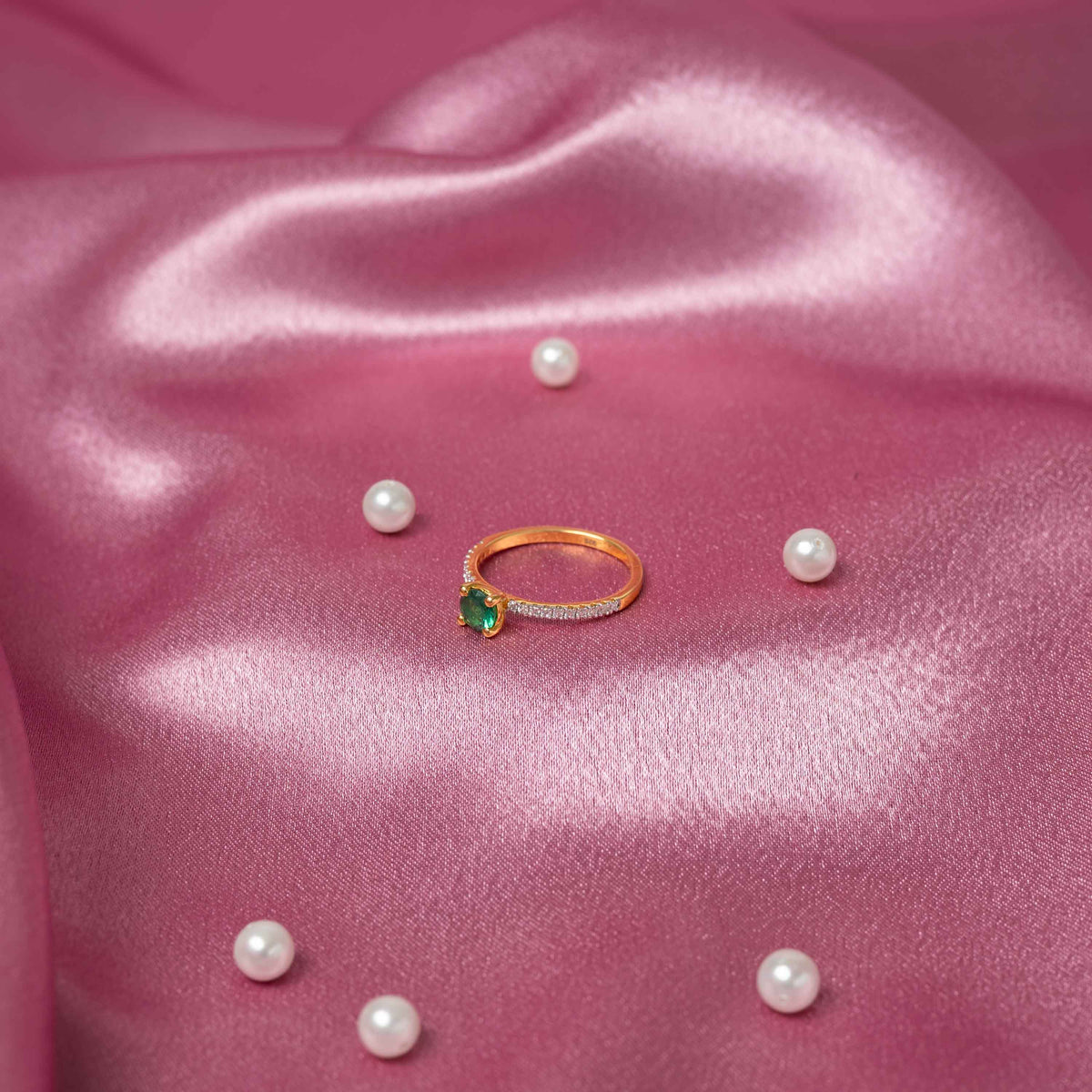 Angled view of three green stones stepped across the CZ pave of a gold plated silver ring