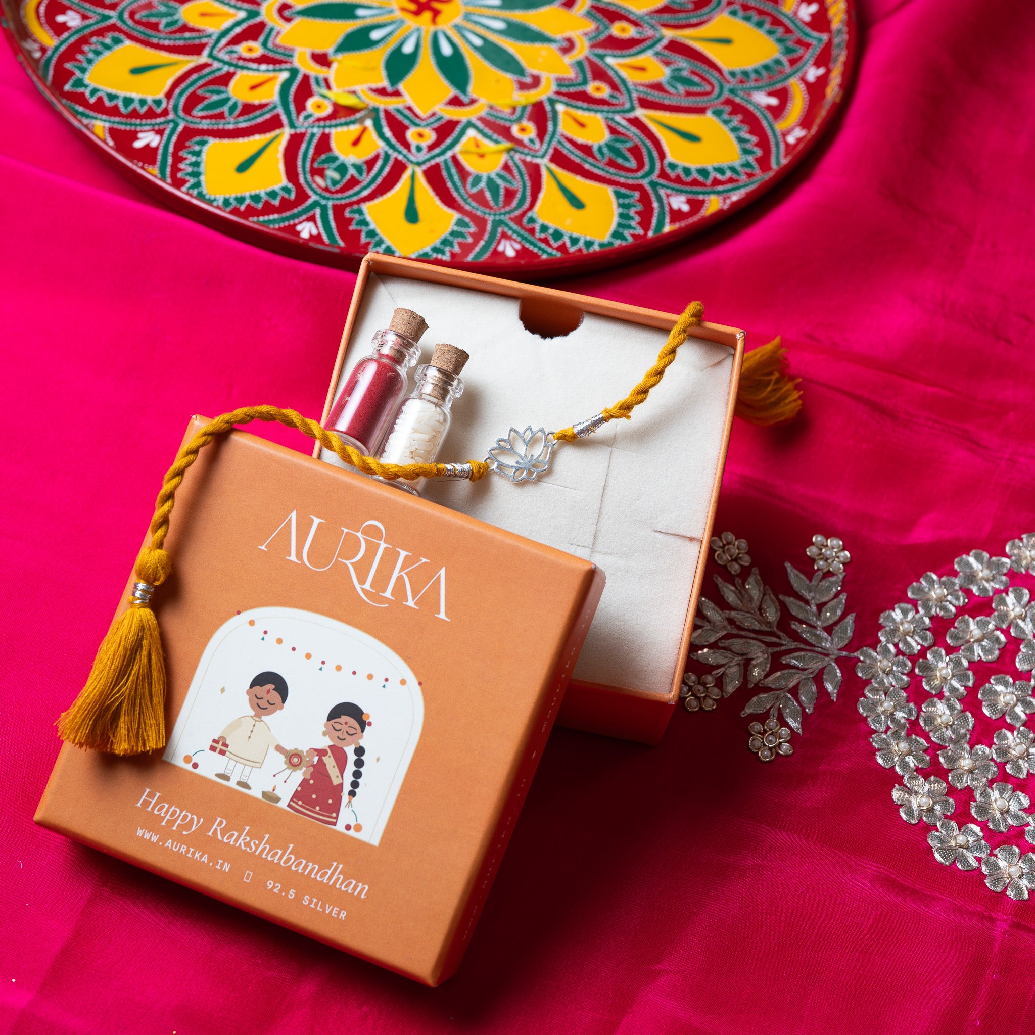 Lotus rakhi with its marigold cord in an open Aurika gift box on rani pink cloth