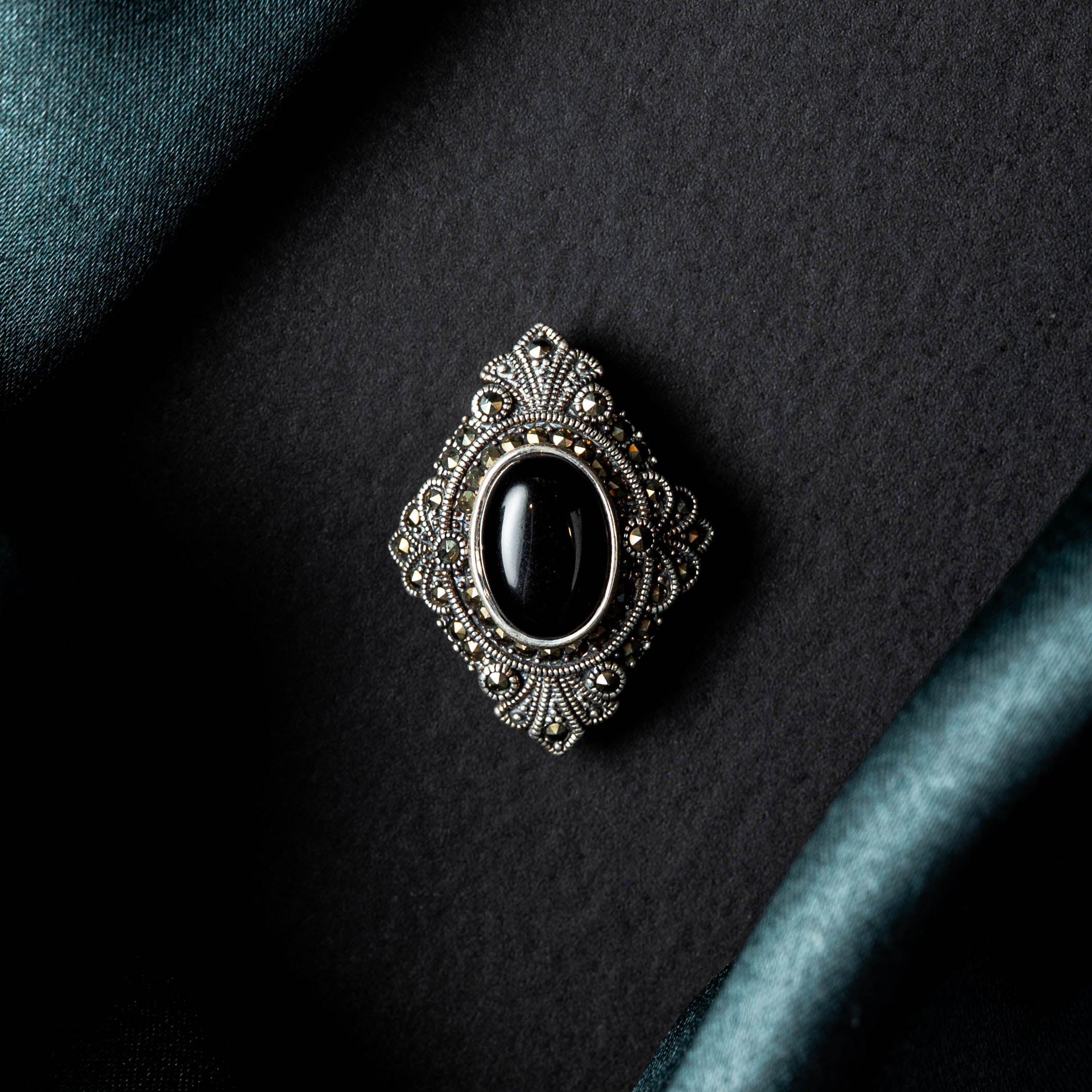 Oxidised rhombus brooch with black onyx centre resting front up on teal satin