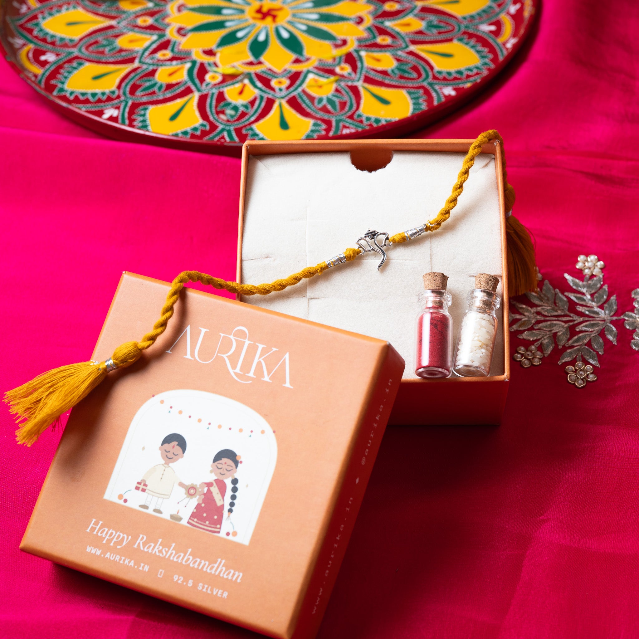 Ganesha rakhi with its marigold cord in an open Aurika gift box on rani pink cloth