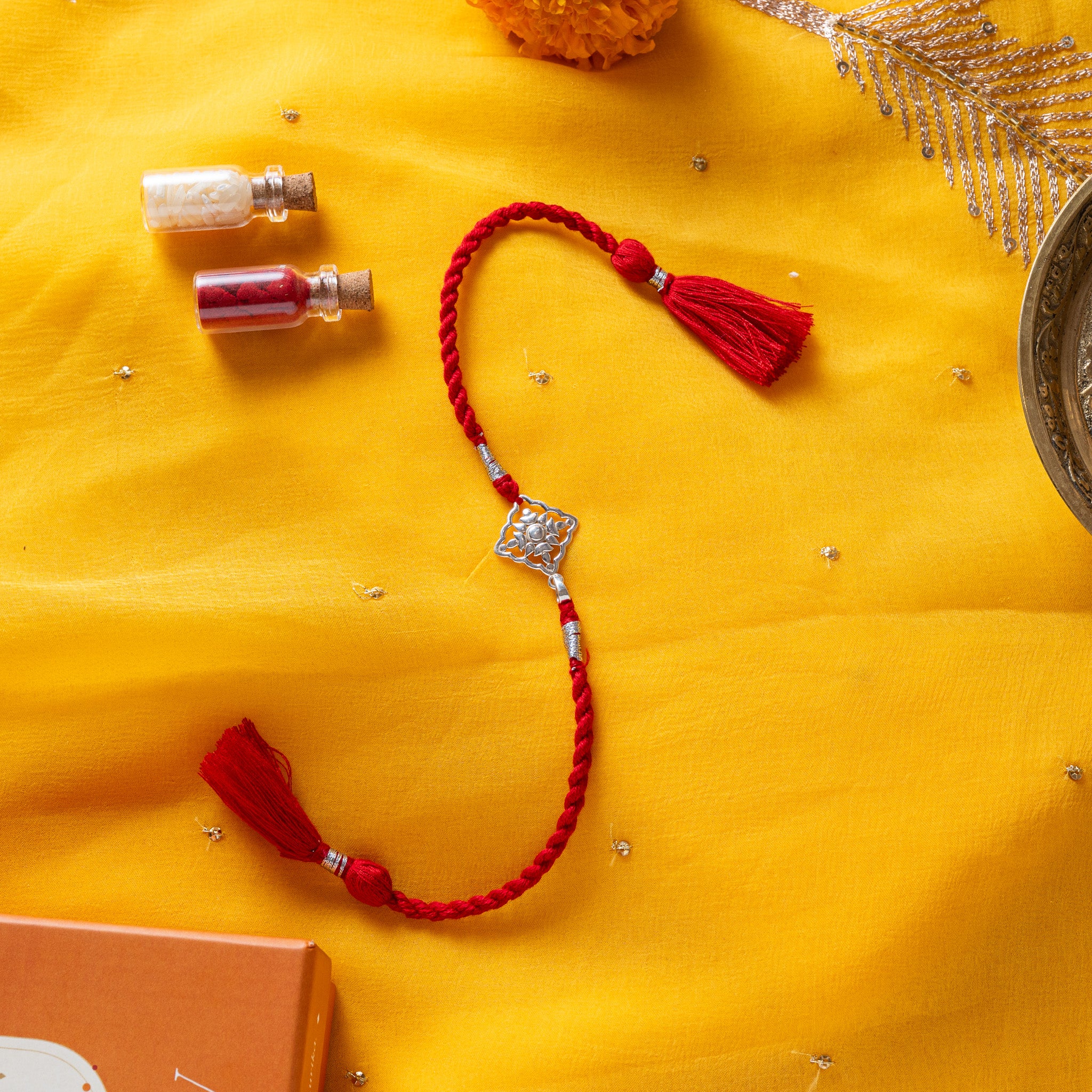 Juhi flower rakhi in 925 silver on a marigold yellow silk cord, on rani pink cloth