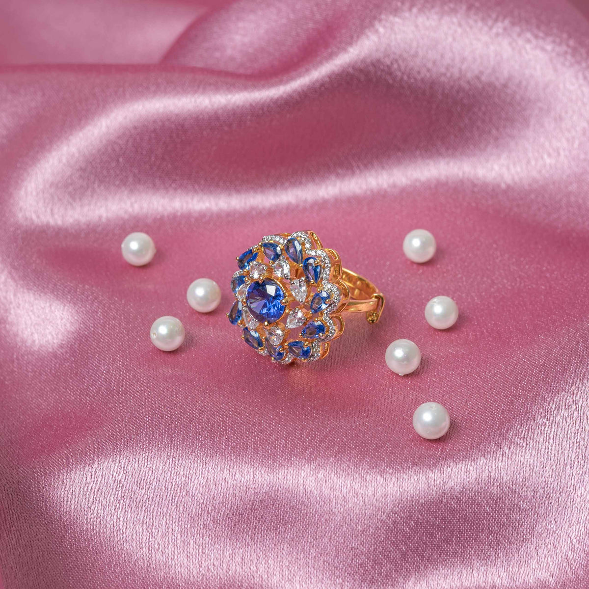 Angled view of blue pear petals opening around CZ pave on a gold plated cocktail ring
