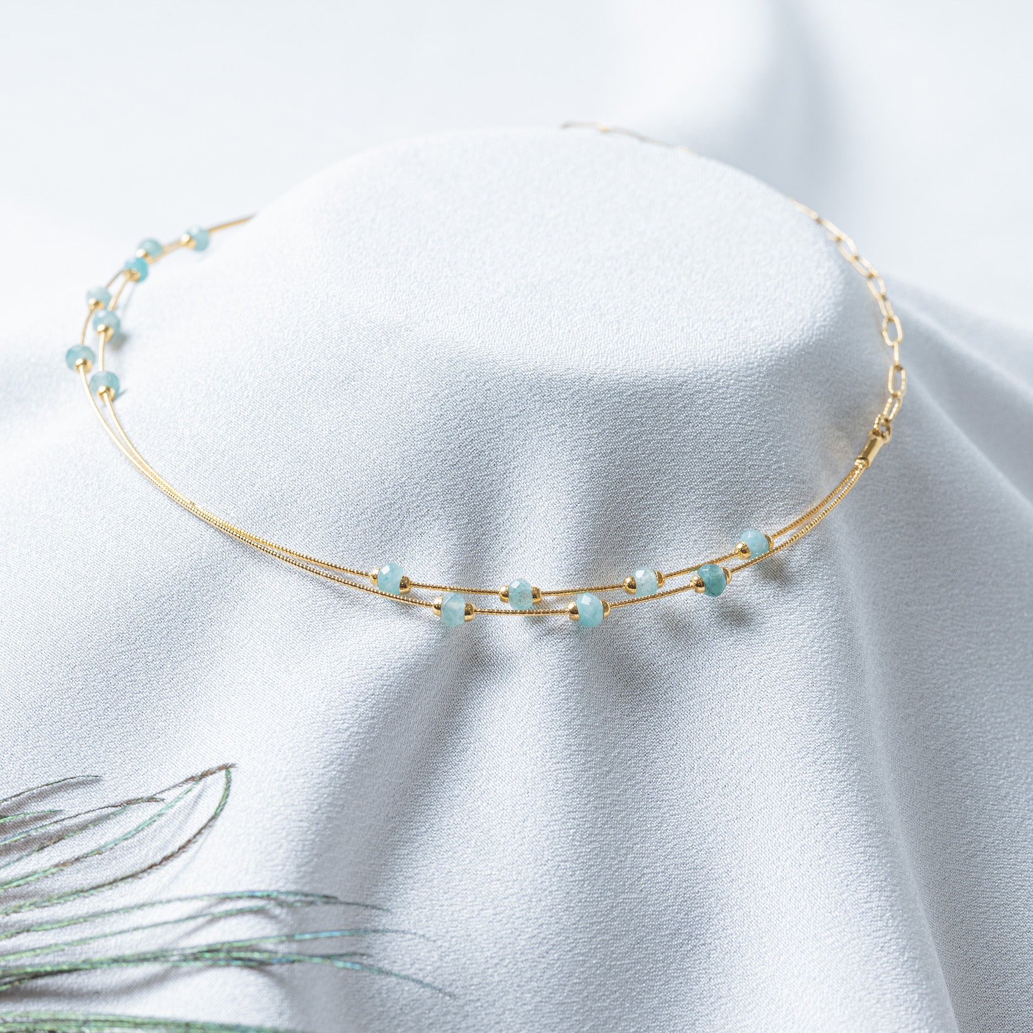 Close crop of semi translucent pale aqua beads capped in gold along the snake strands