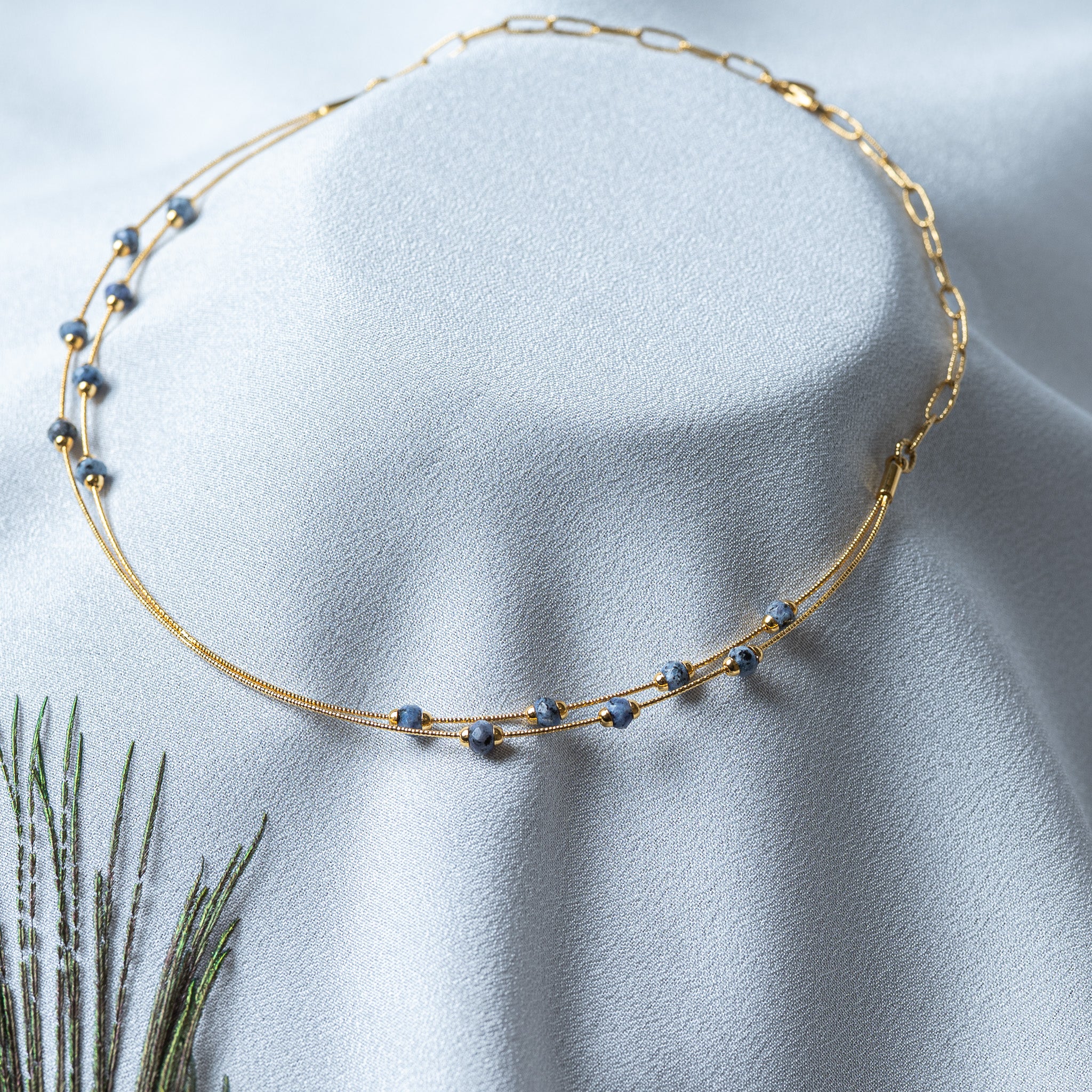 Close crop of one opaque blue grey bead pinched between two tiny gold caps