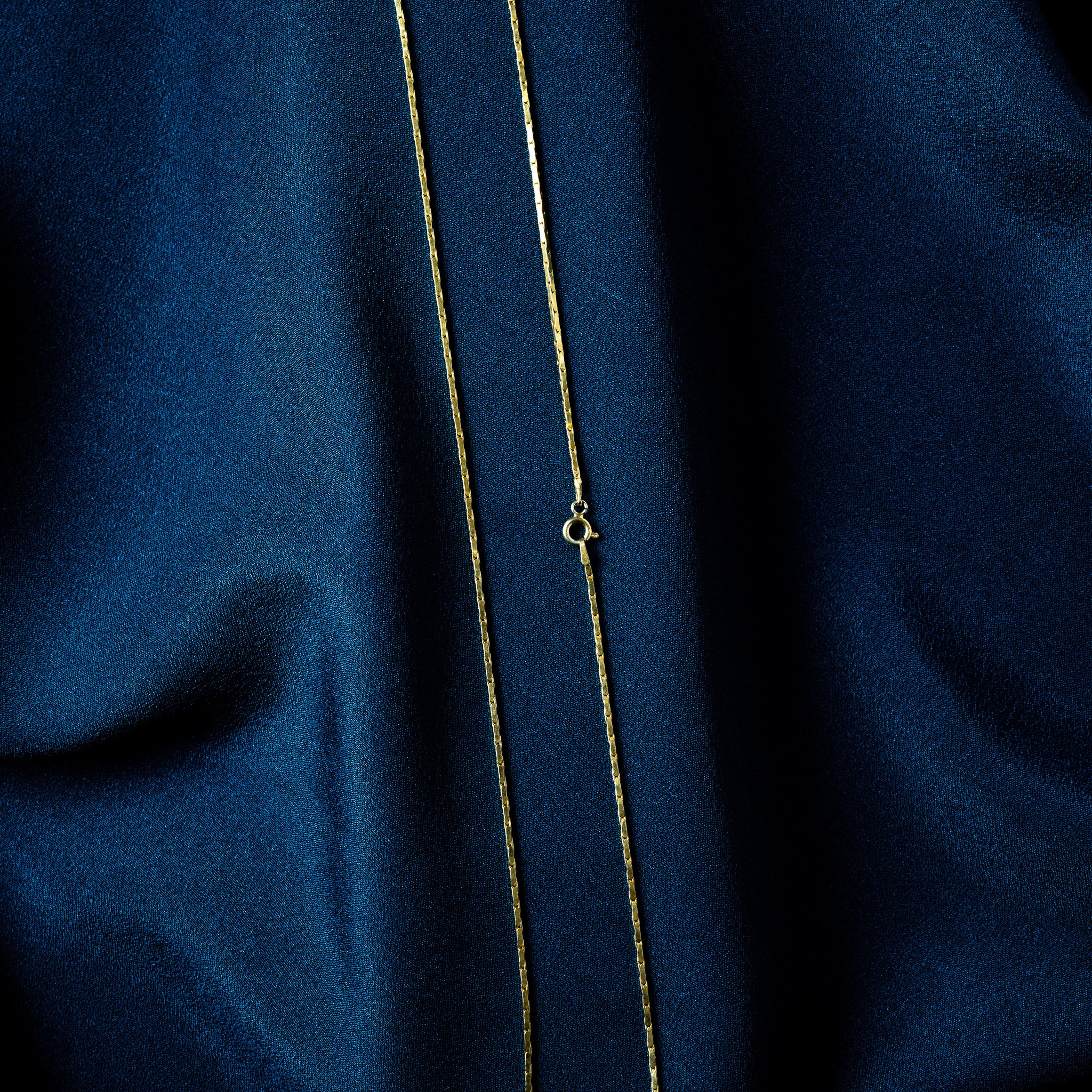Spring ring clasp with its thumb tab on a gold bar link chain, close crop