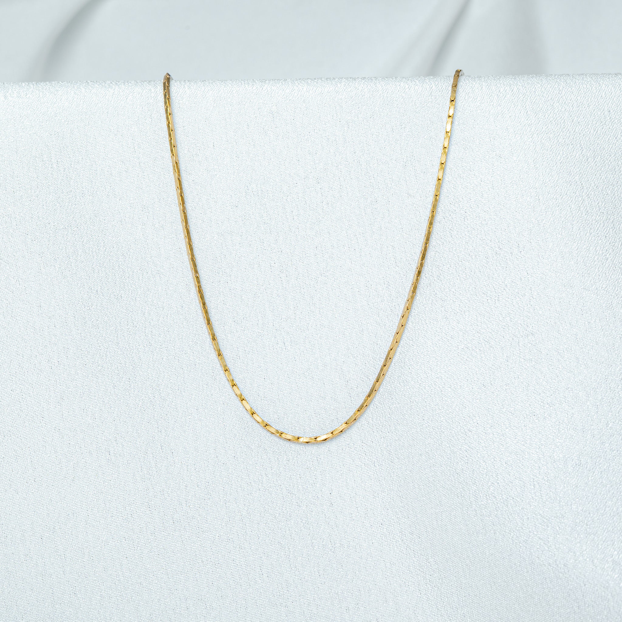 Close crop of a gold flat link chain, wide lozenge segments reading as a flattened rope