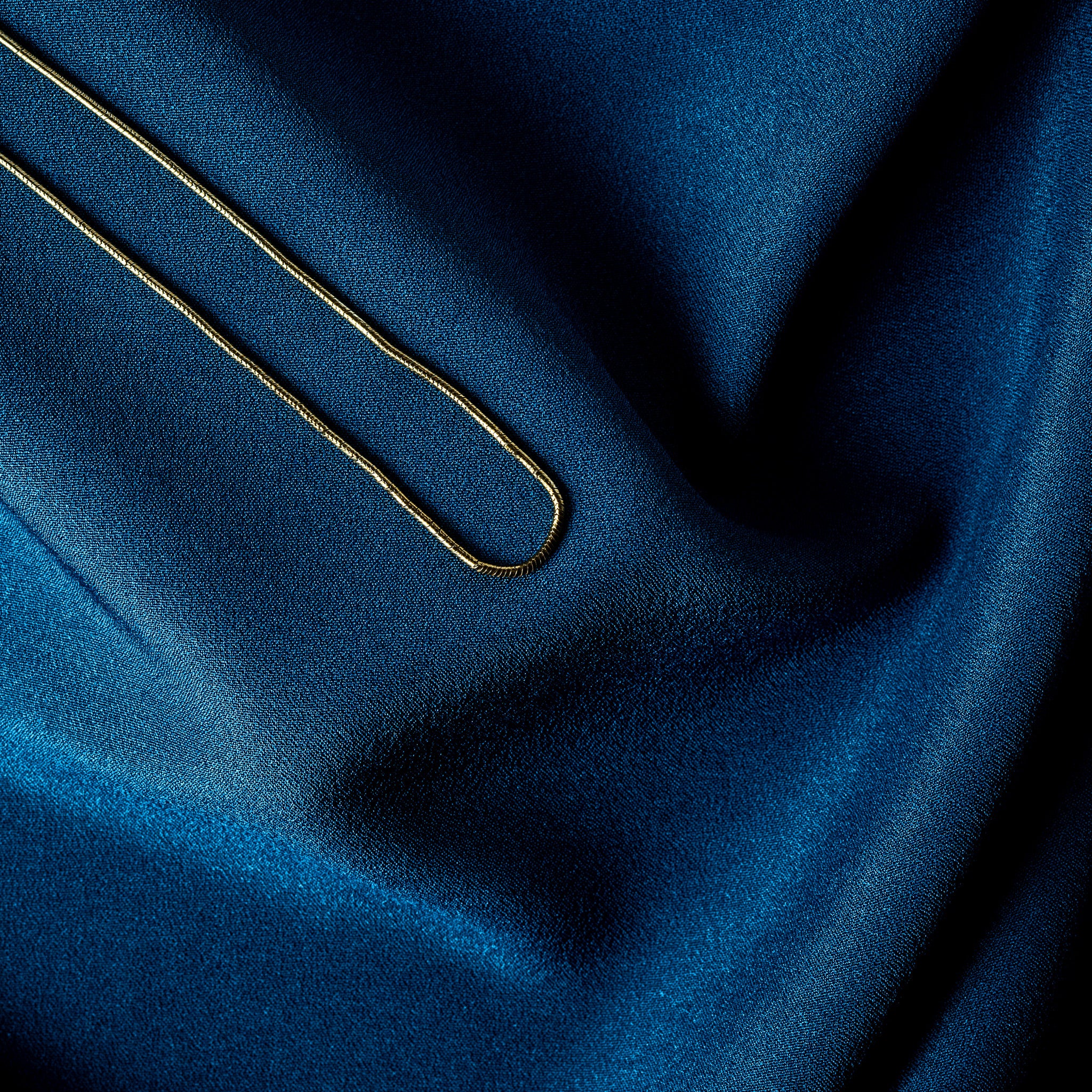 Crimped tubular cap and lobster clasp on a gold snake chain, fastening macro