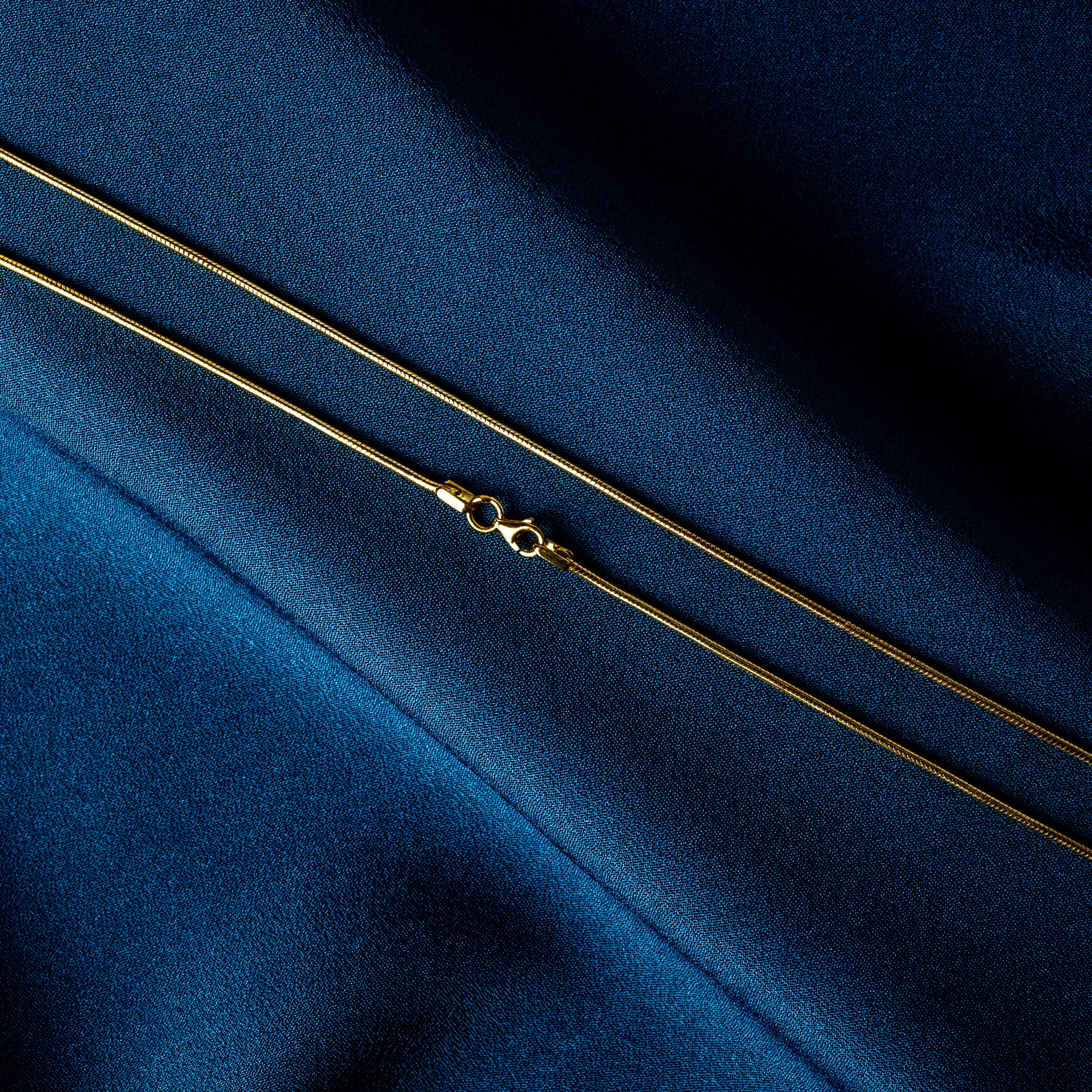 Lobster clasp and solid cylindrical end cap on a gold plated snake chain, close crop