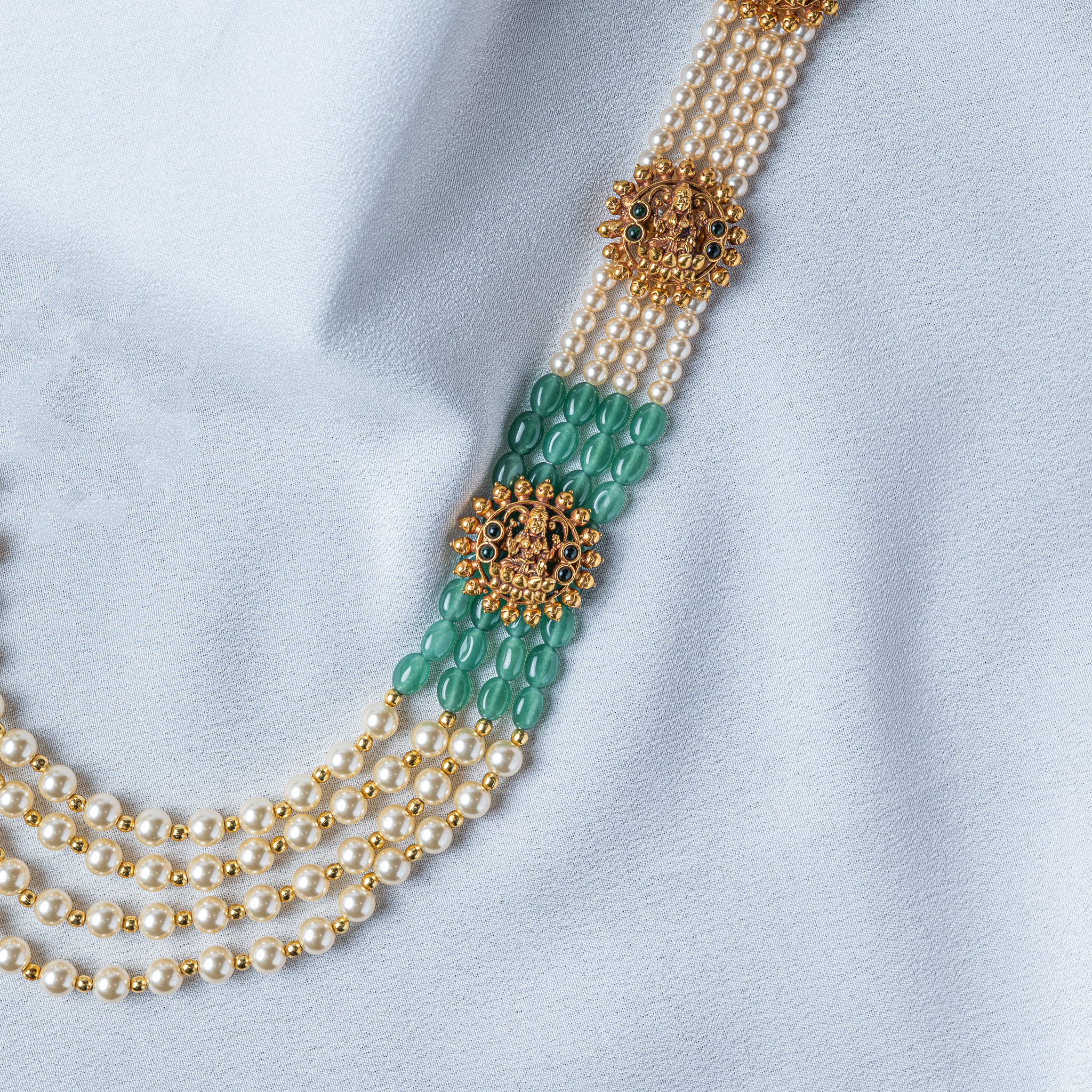 Seated Lakshmi in a granulated gold motif ringed with green and dark stones, close crop