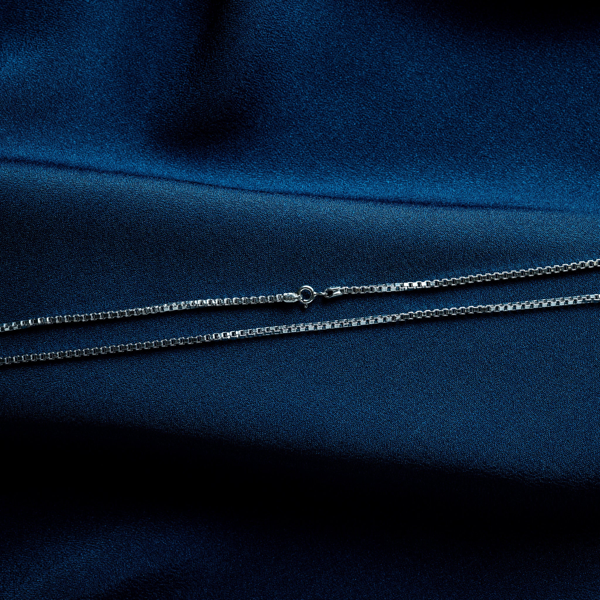 Close crop of a silver box chain, square links stacked with mirrored faces