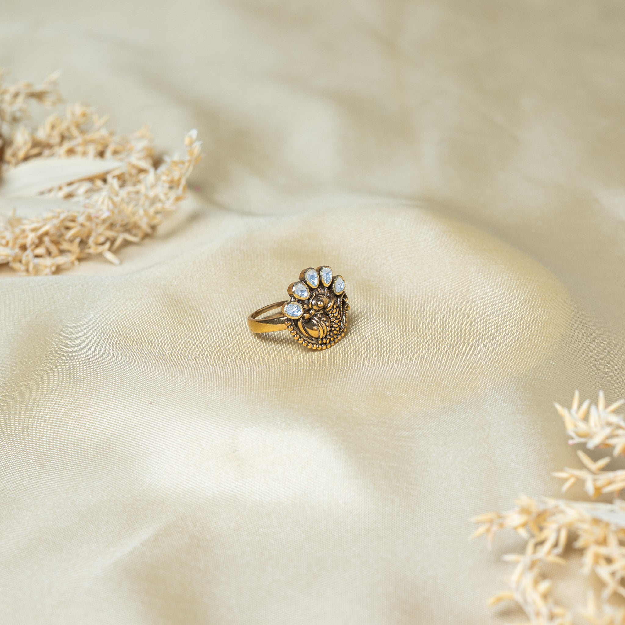Angled view of the peacock head, its domed eye and the beaded gold border of the ring face