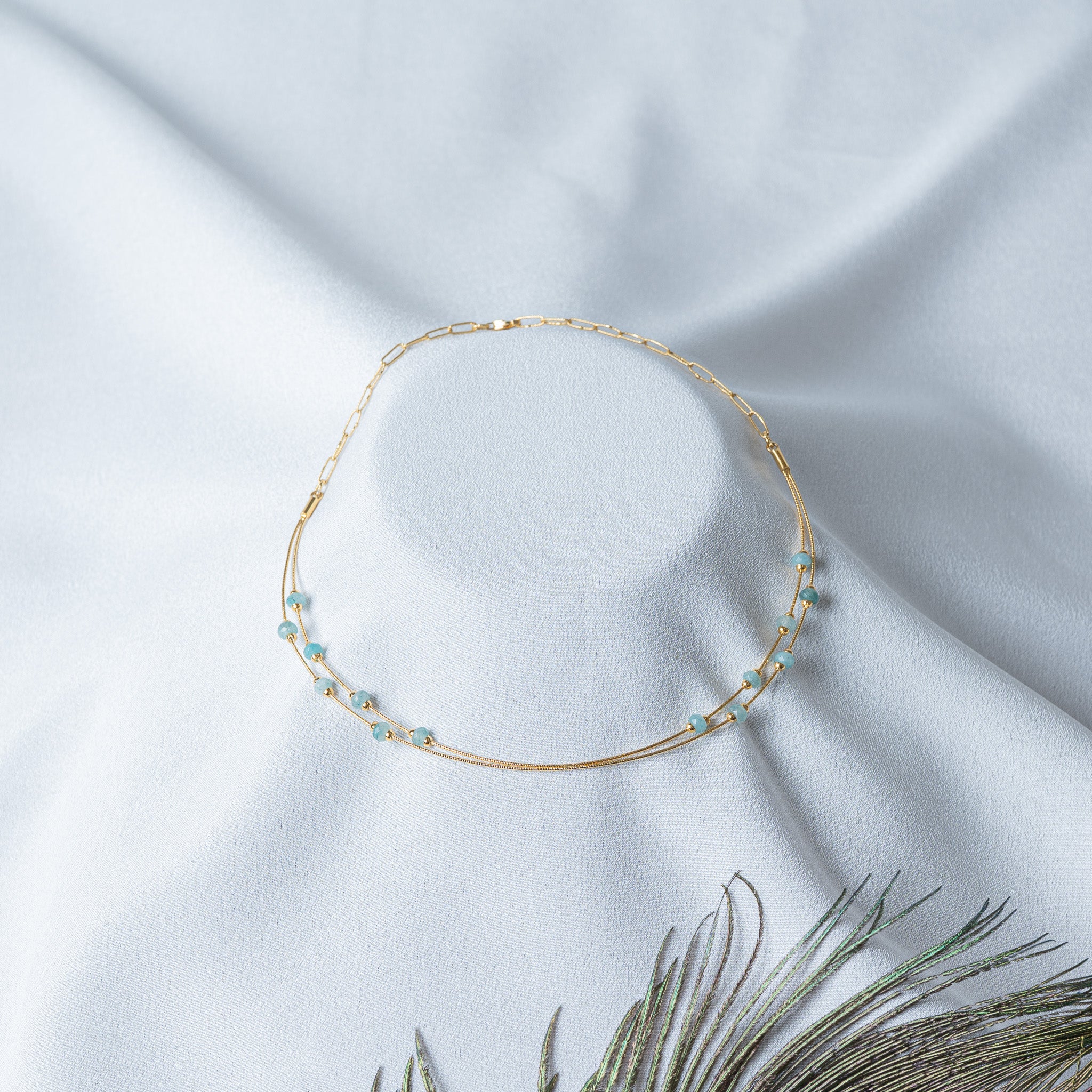 Angled view of the double strand gold collar with aqua bead stations offset
