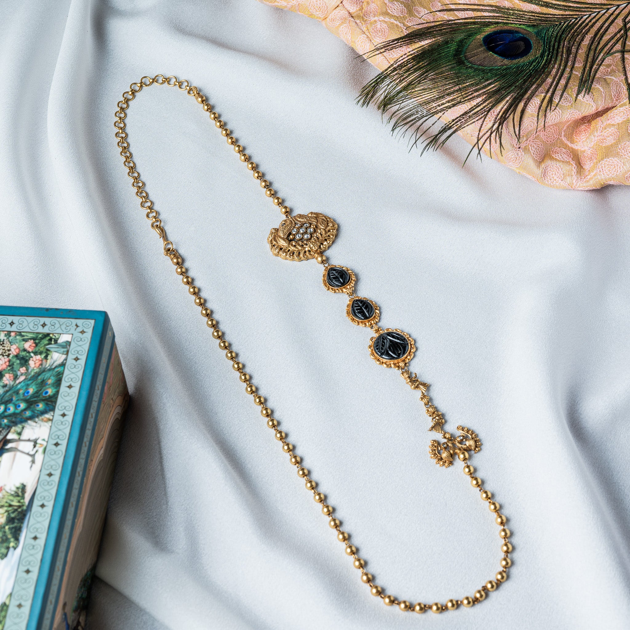Side view of three leaf carved black onyx stones stepping down the gold ball chain