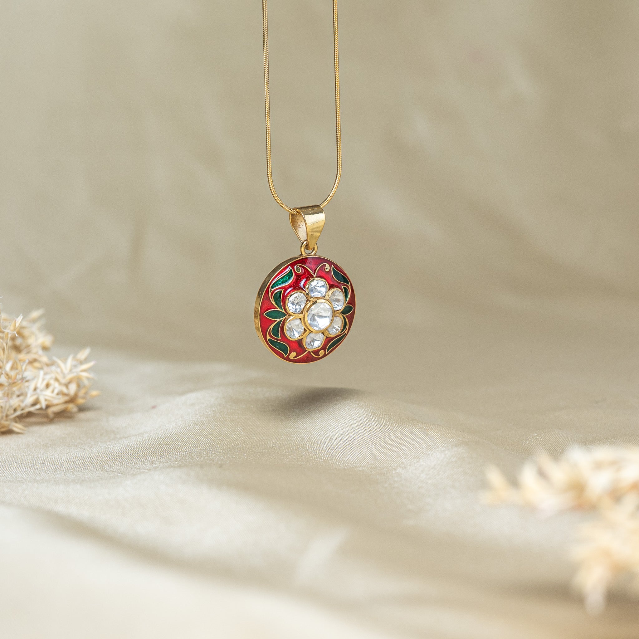 The red meenakari disc at an angle, showing the depth of the gold rim and the flat top loop
