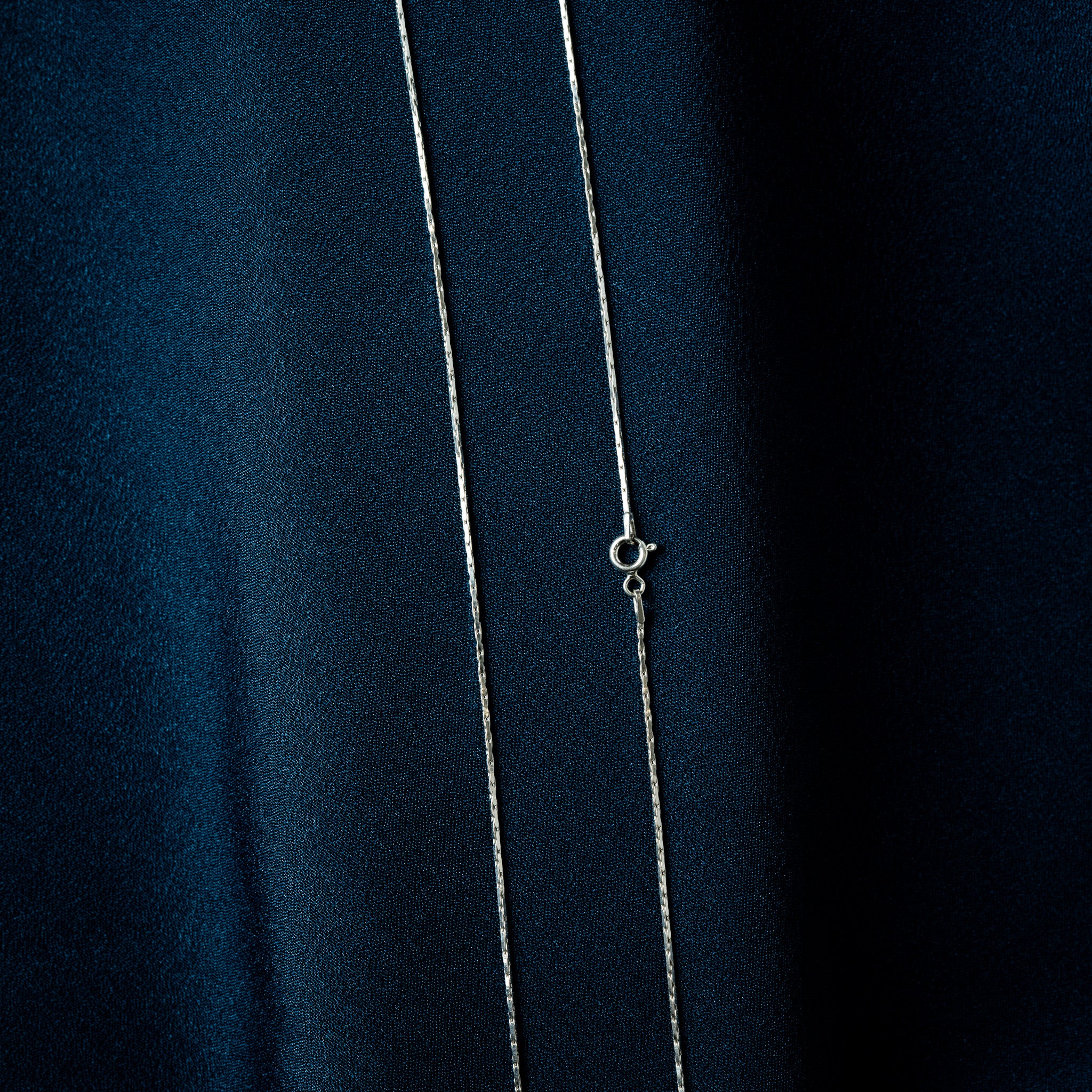 Close crop of a fine silver chain showing the faceted bar links and wavy edge