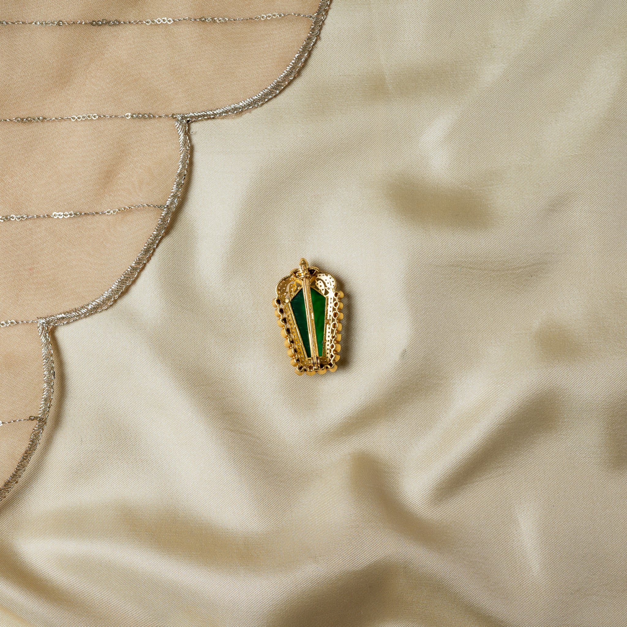 Angled reverse showing the open setting behind the carved green stone and the raised steel pin