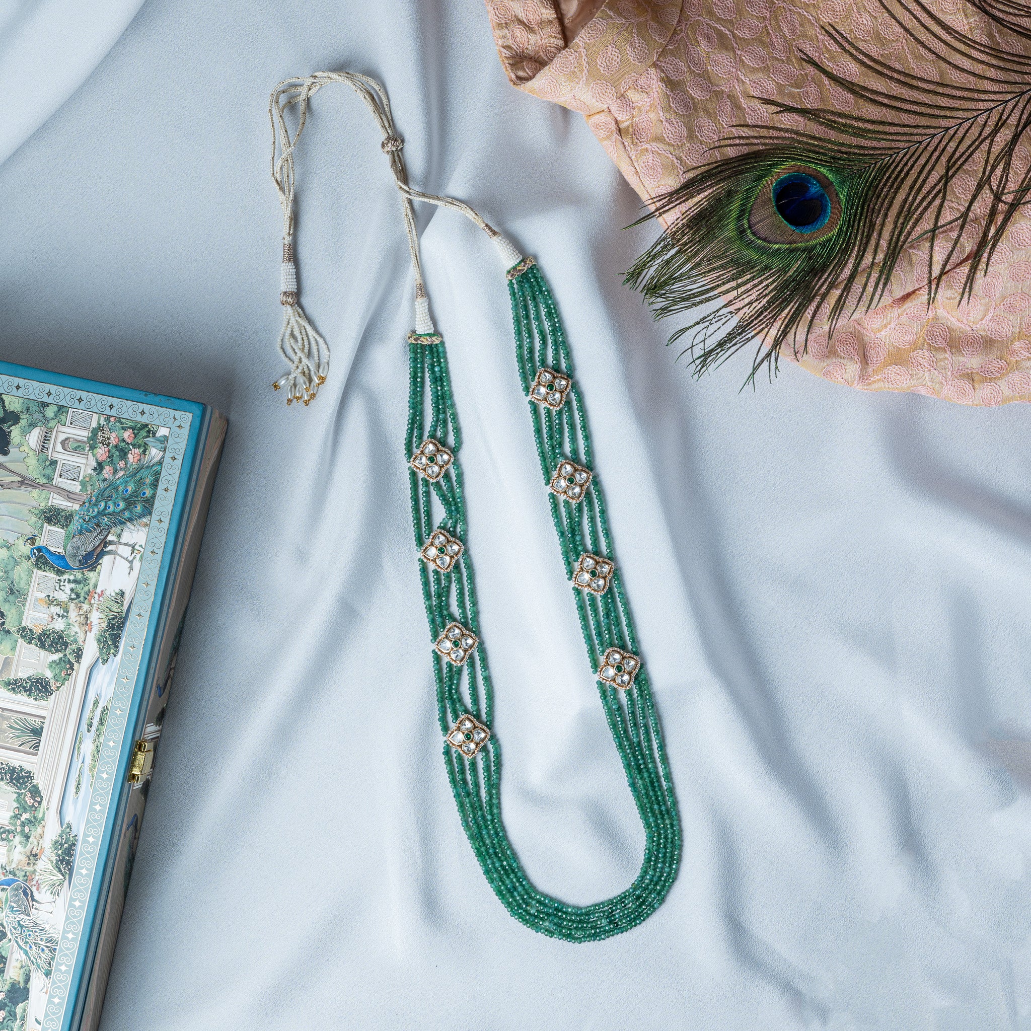 Green bead necklace laid flat with the braided cord and tassel drawn out