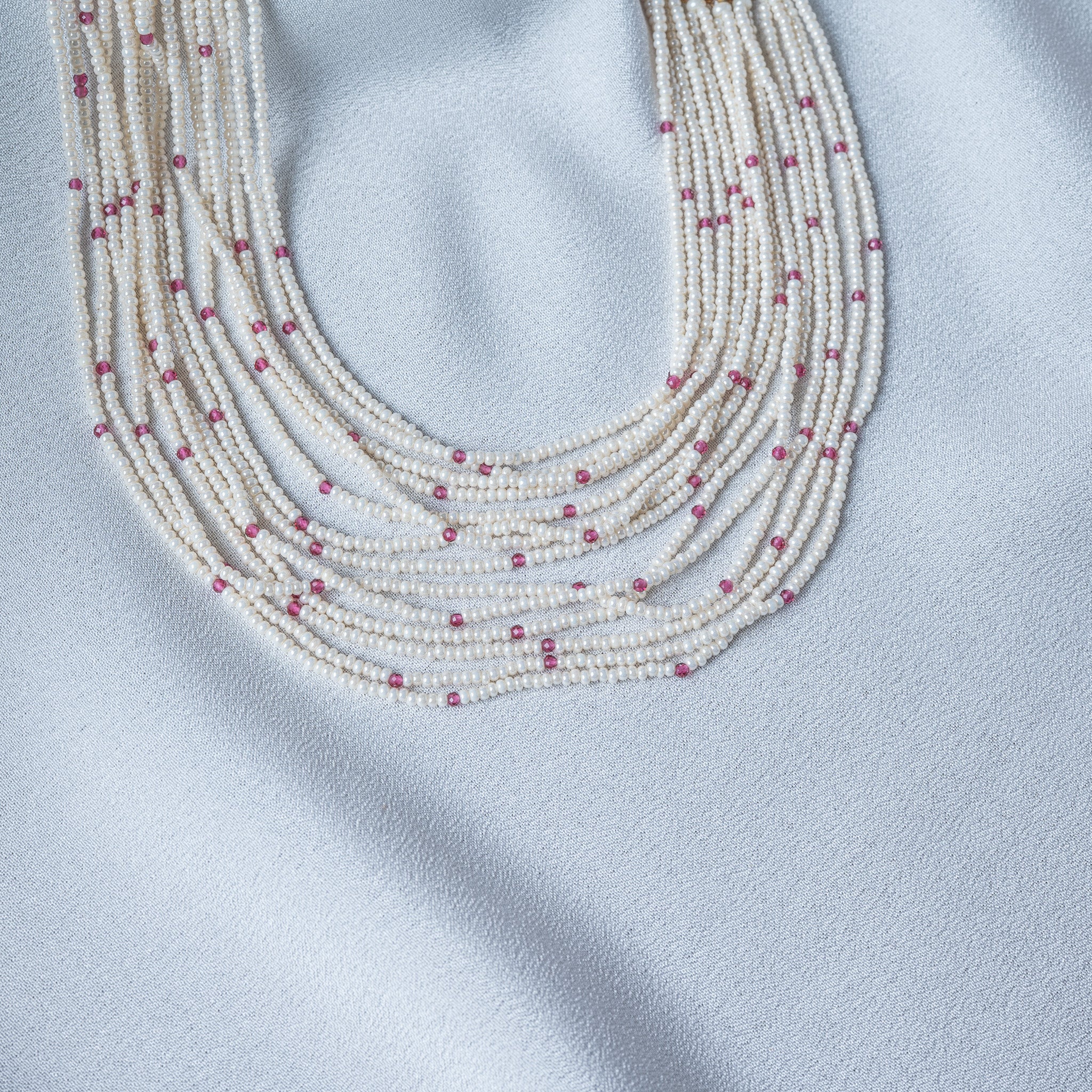 Faceted red beads scattered between the rice pearl strands, seen close
