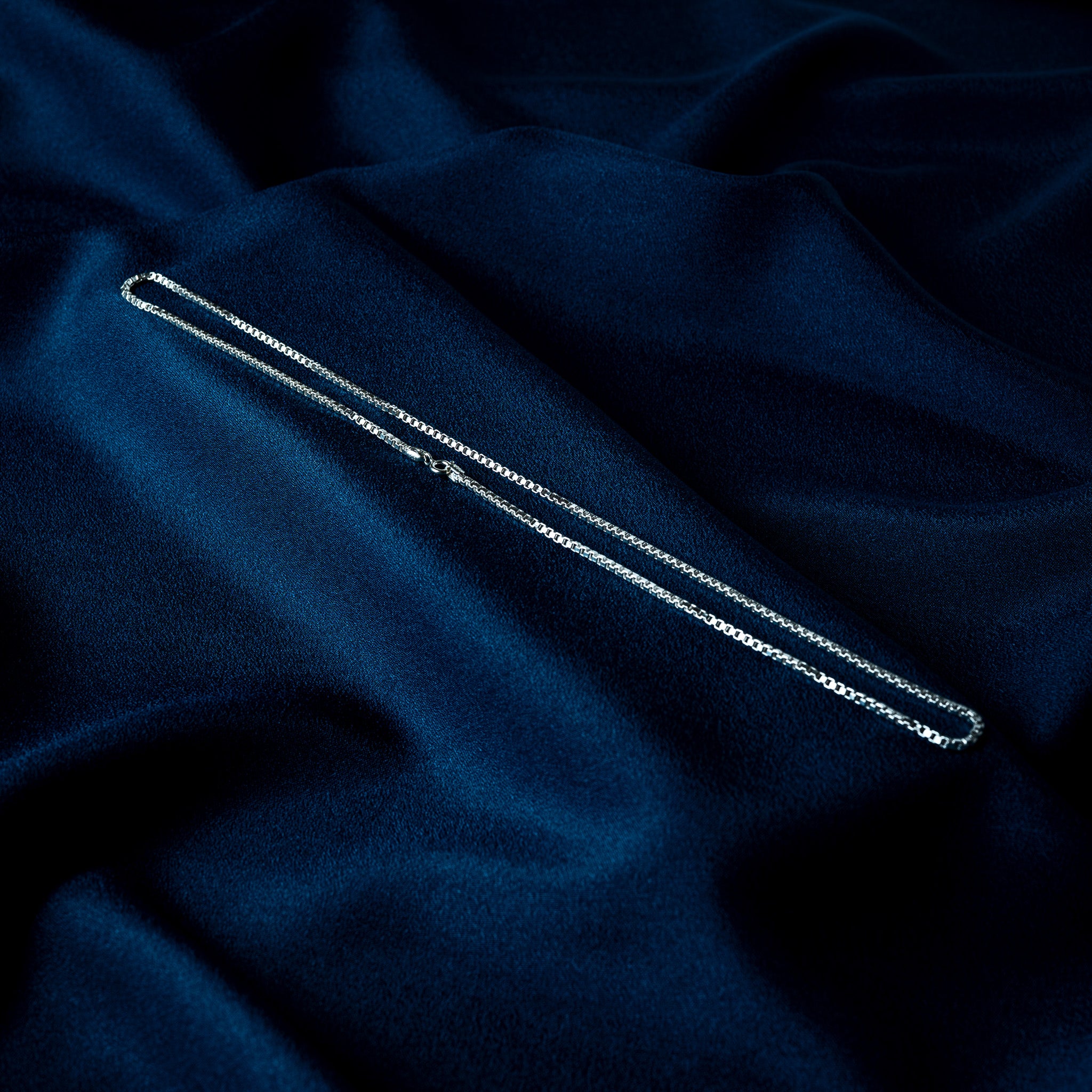 Twenty inch silver box chain laid out flat, squared venetian links throughout