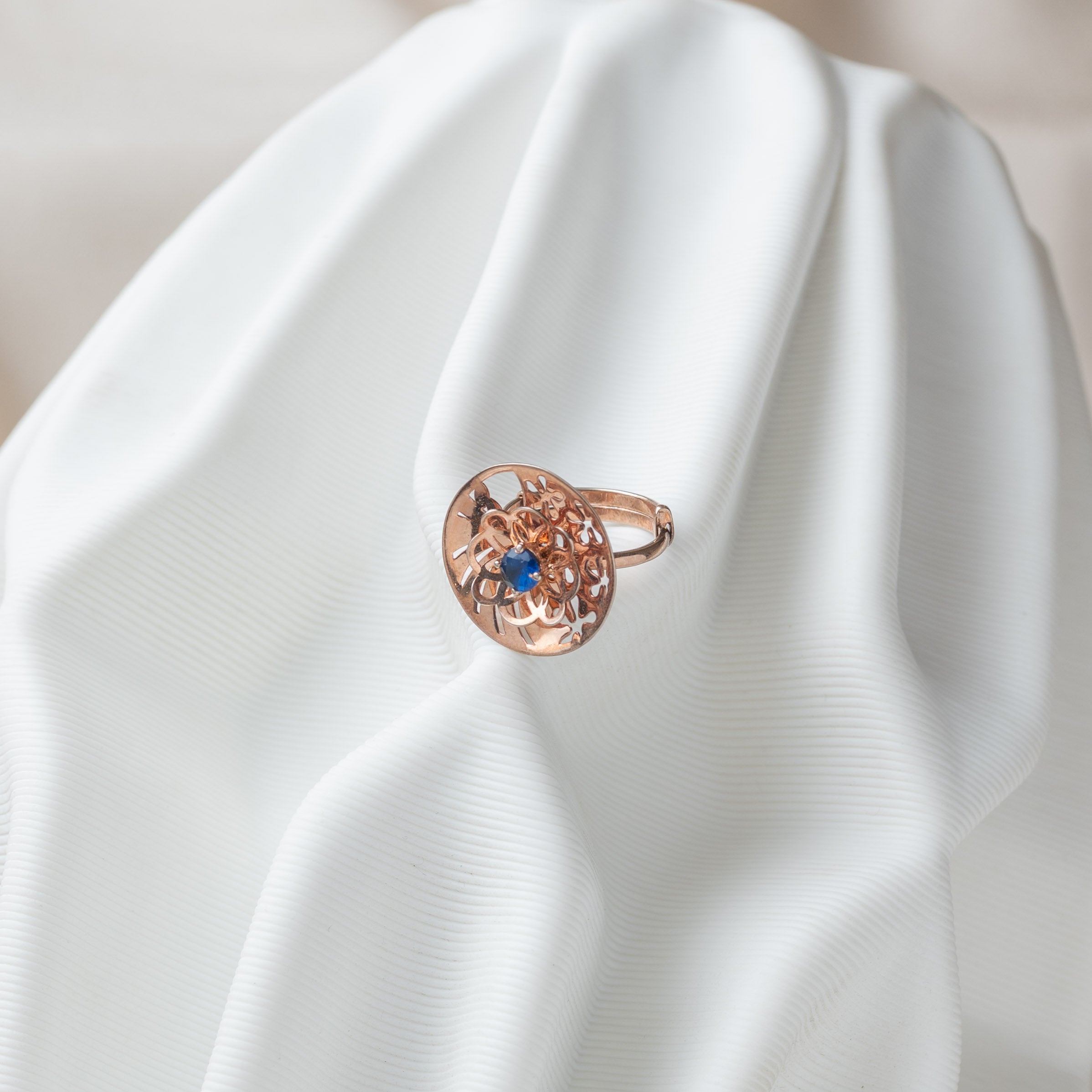 Angled view of the cut through jaali disc and its blue sapphire, rose gold plated 925 silver