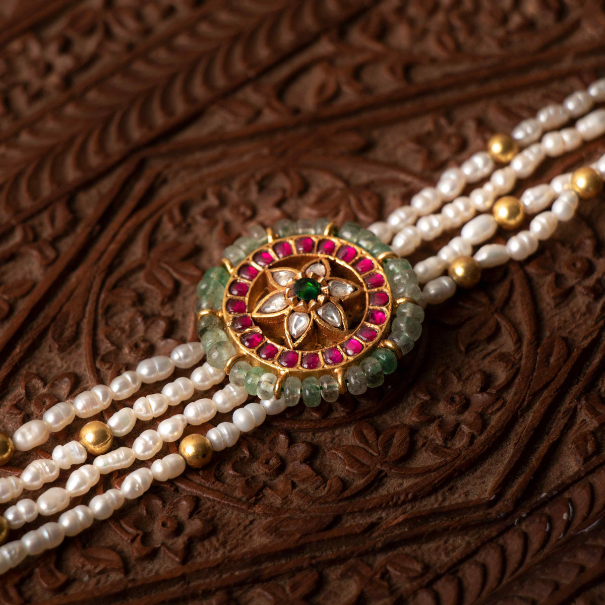 Round kundan medallion sitting between four rows of rice pearls, seen at an angle