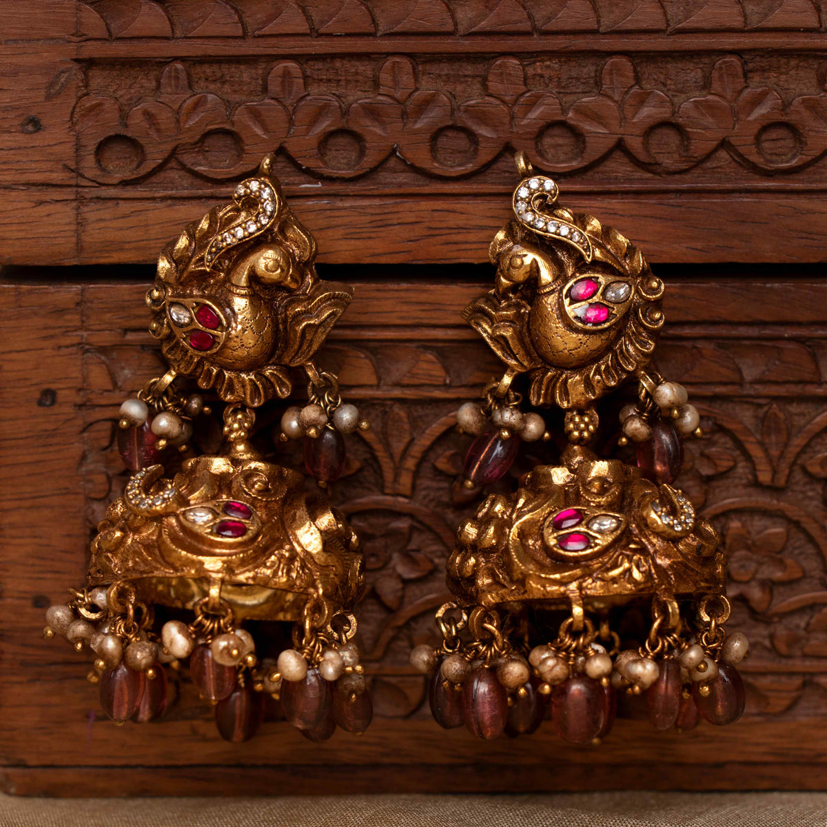 Nakaashi peacock jhumkas with carved dome, maroon bead and grey pearl drops, antique gold plated silver.