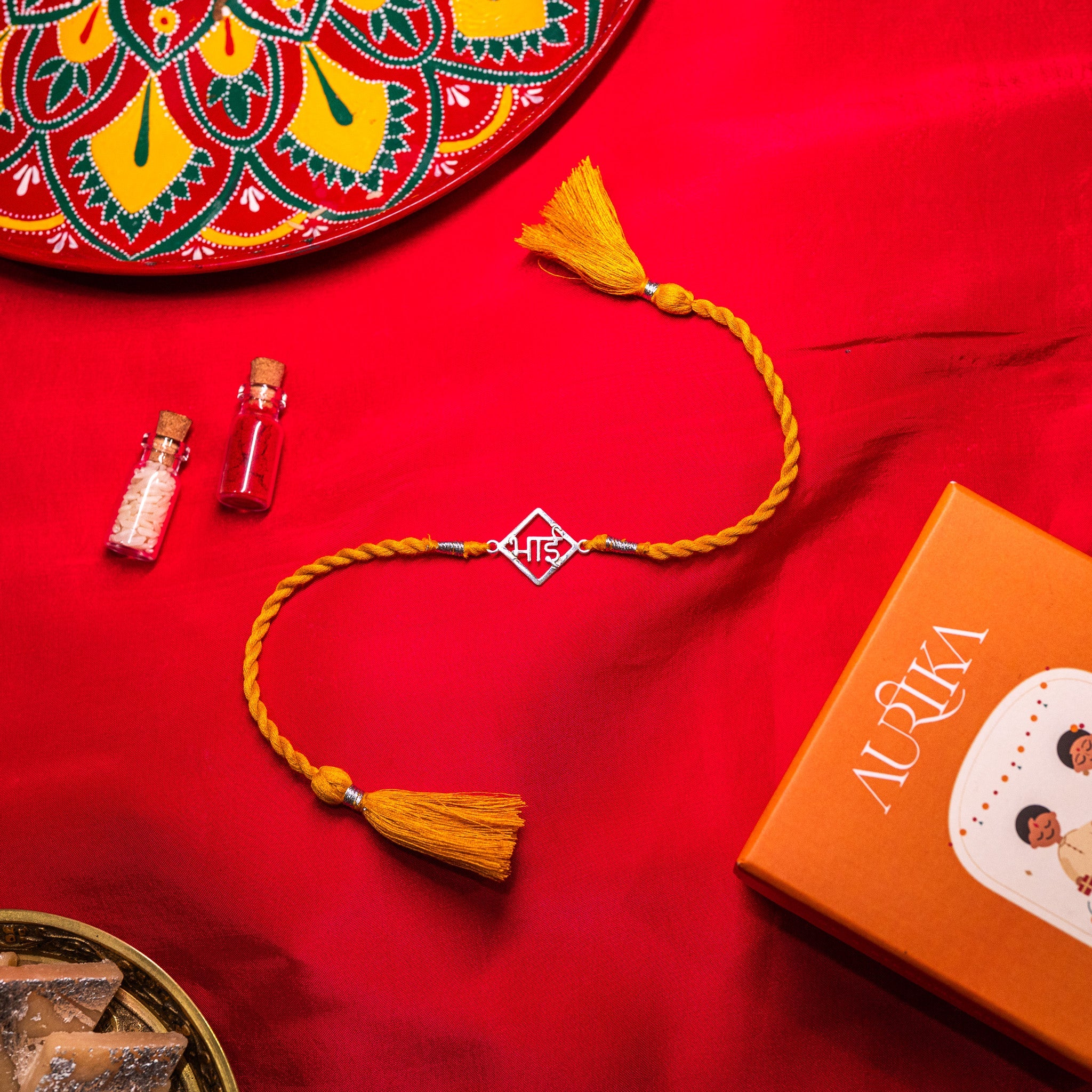 Bhai lettering rakhi in 925 silver on a marigold yellow silk cord, on rani pink cloth