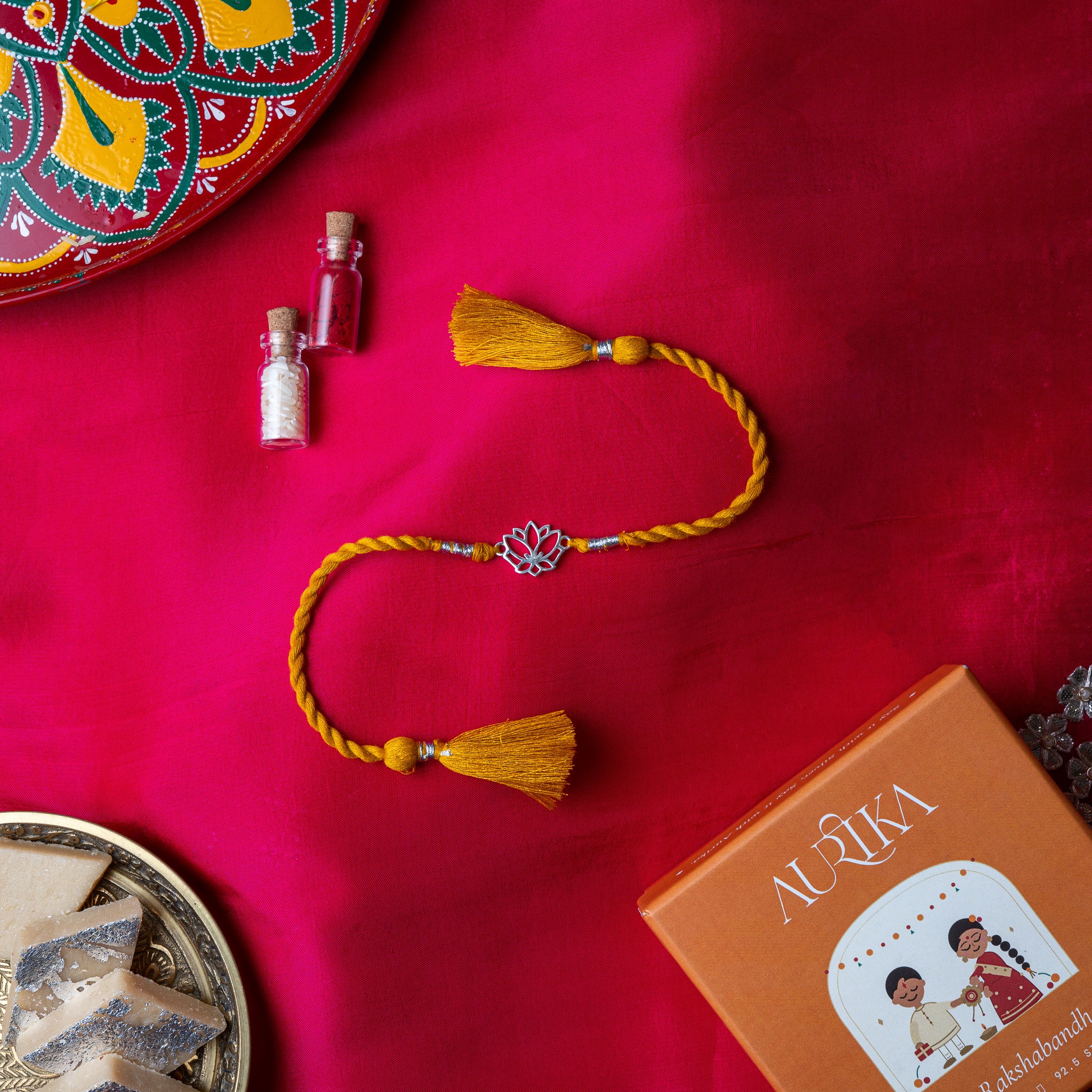 Lotus rakhi in 925 silver on a marigold yellow silk cord, on rani pink cloth