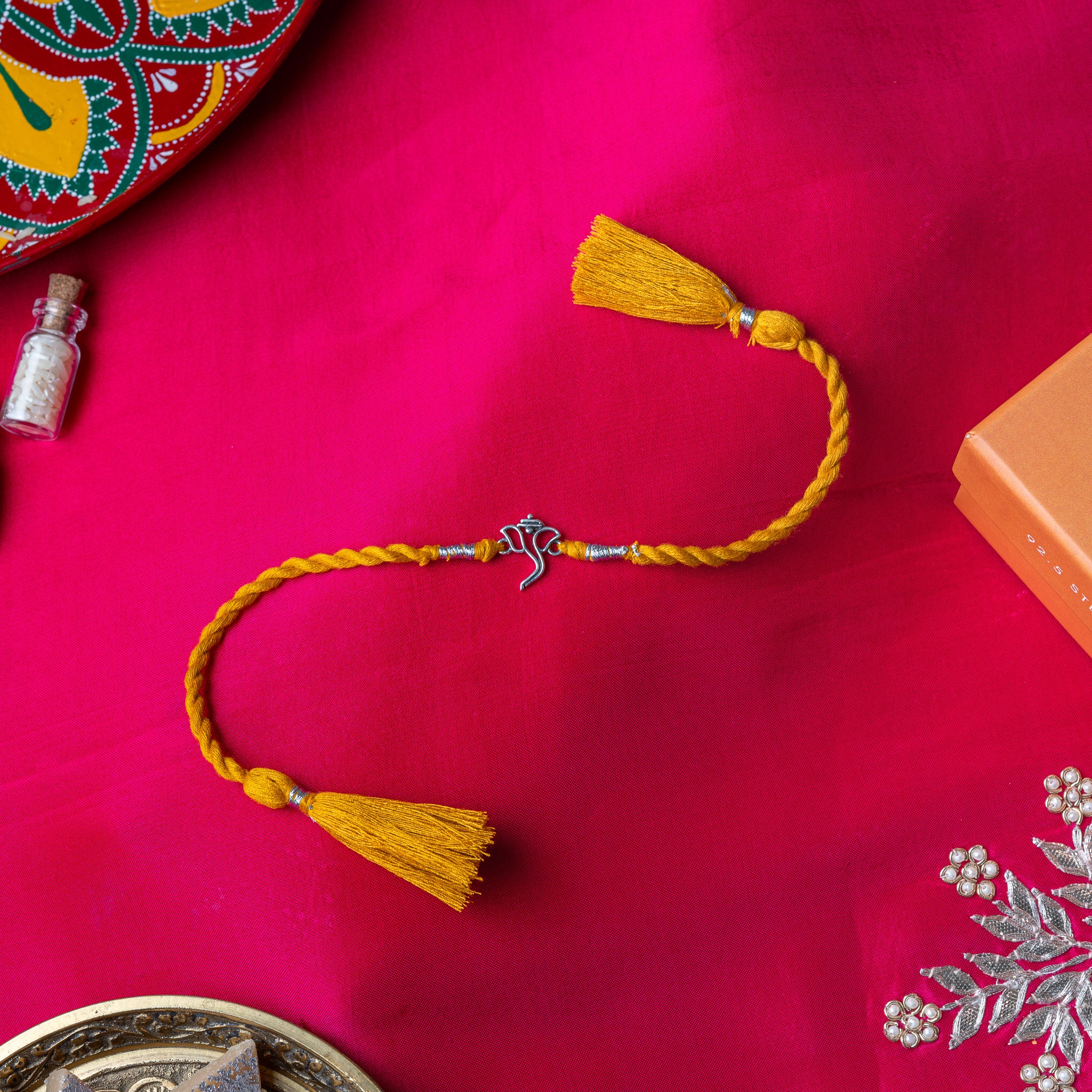 Ganesha rakhi in 925 silver on a marigold yellow silk cord, on rani pink cloth