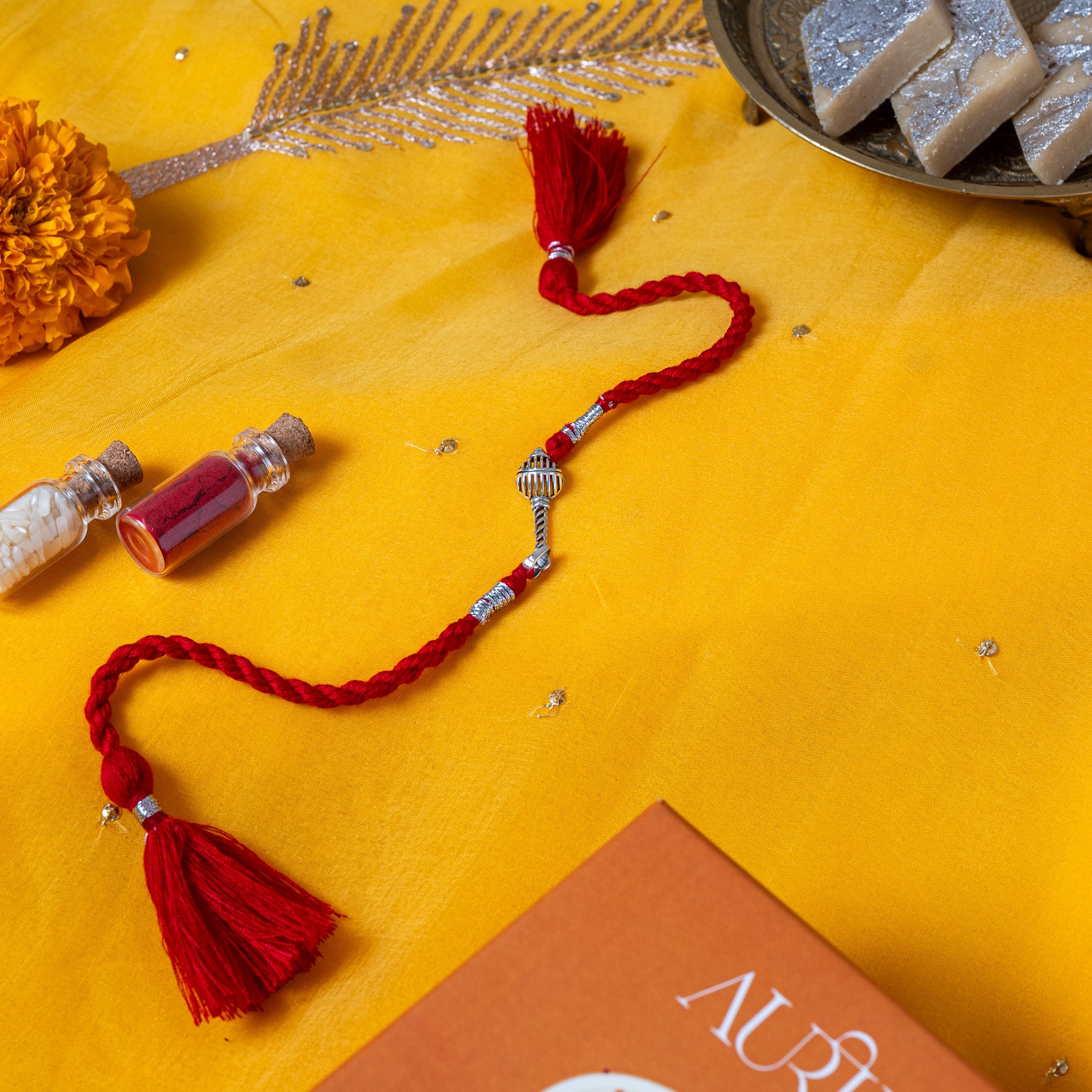 Ribbed gada mace head between two silver caps in 925 silver on a red twisted silk rakhi cord with tassels
