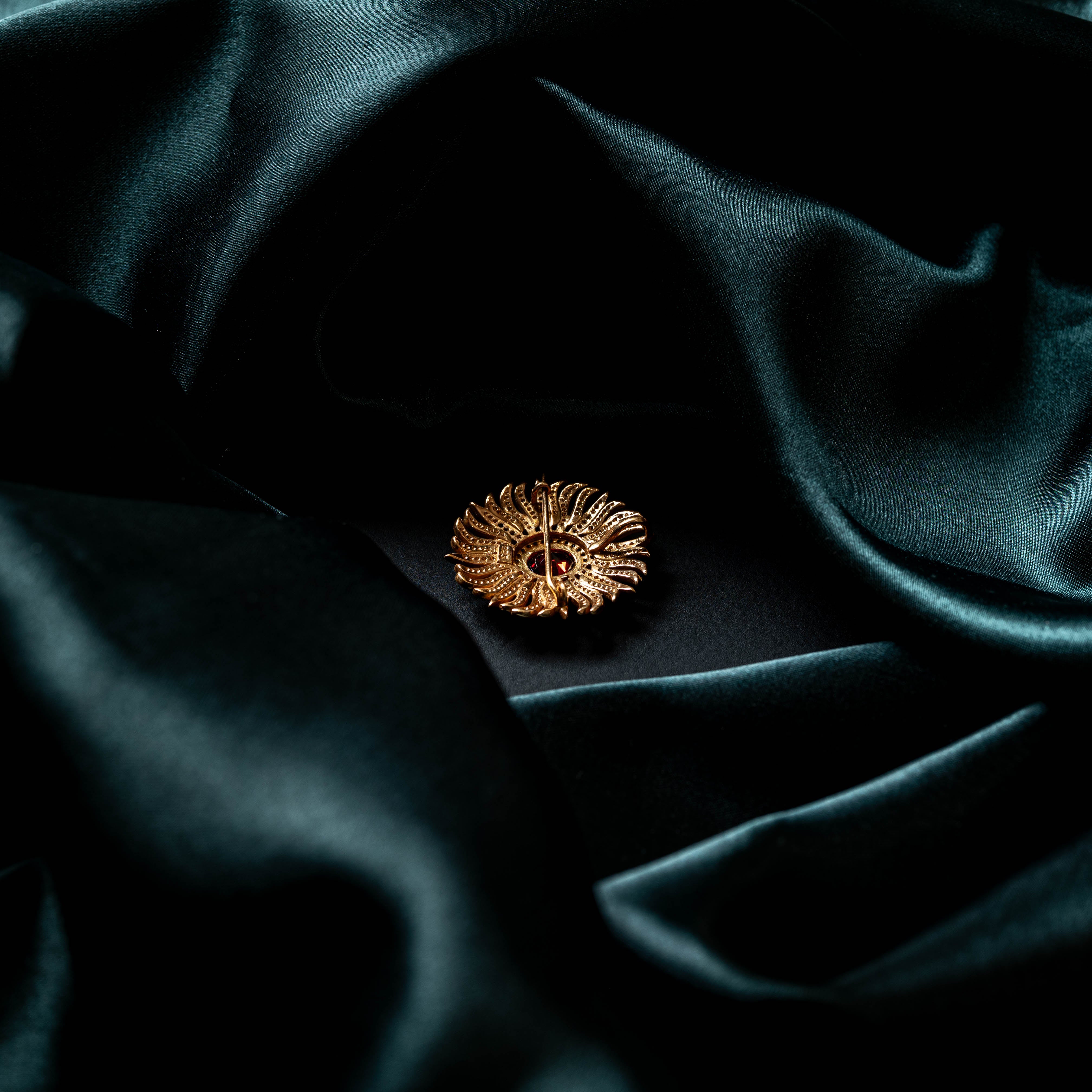 Sunburst brooch with an oval ruby centre and CZ paved rays in gold plated 925 silver on teal satin