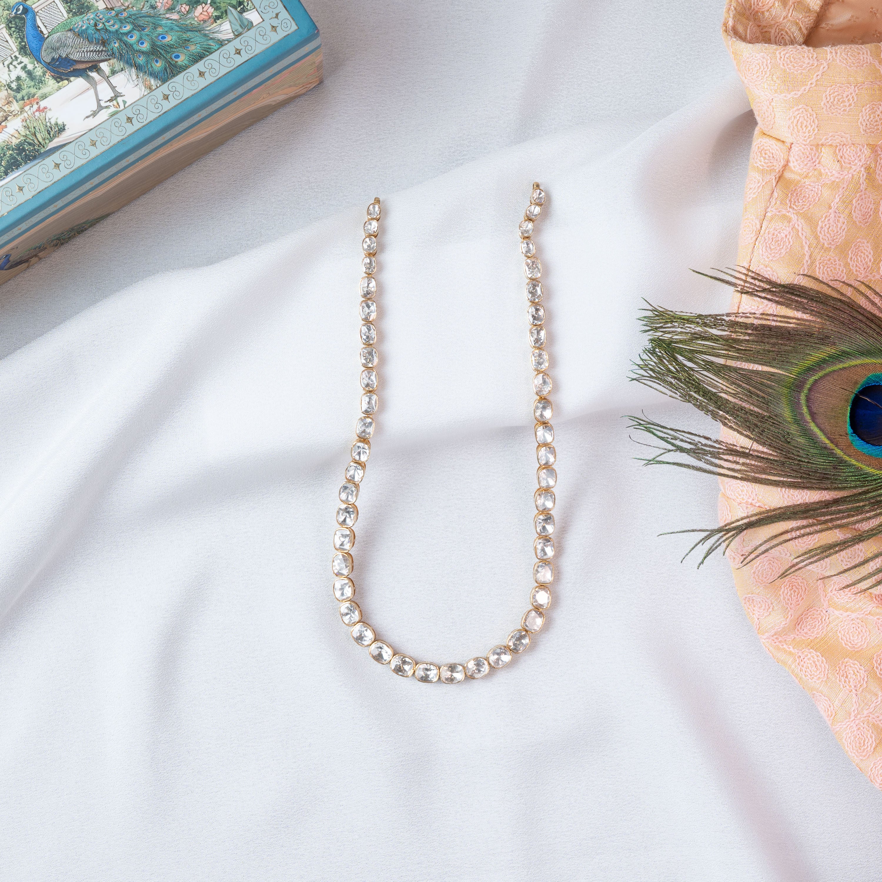 Full length of the single strand polki kantha laid in a U with a peacock feather beside it
