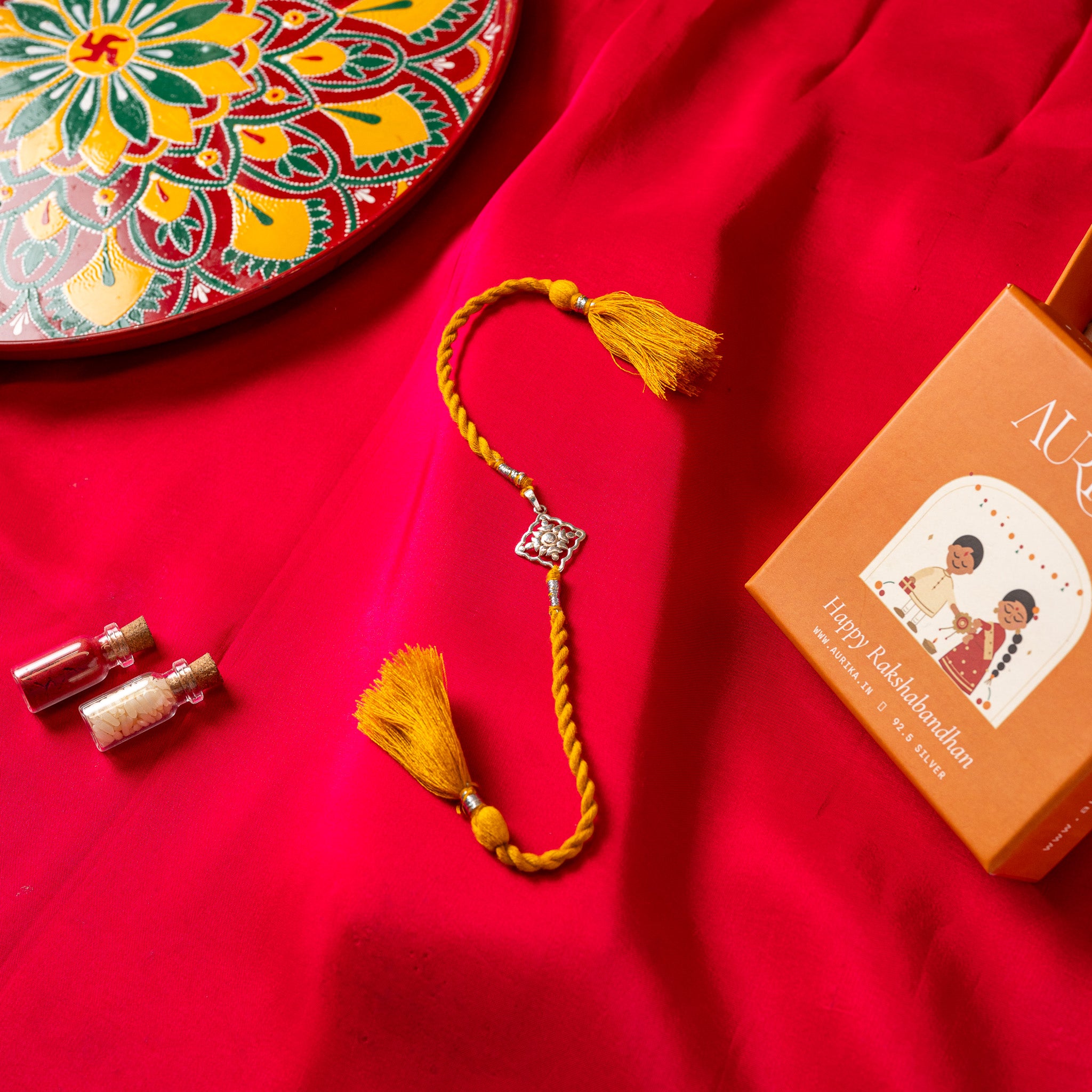 Juhi flower pierced through a square on its point in 925 silver on a red twisted silk rakhi cord with tassels
