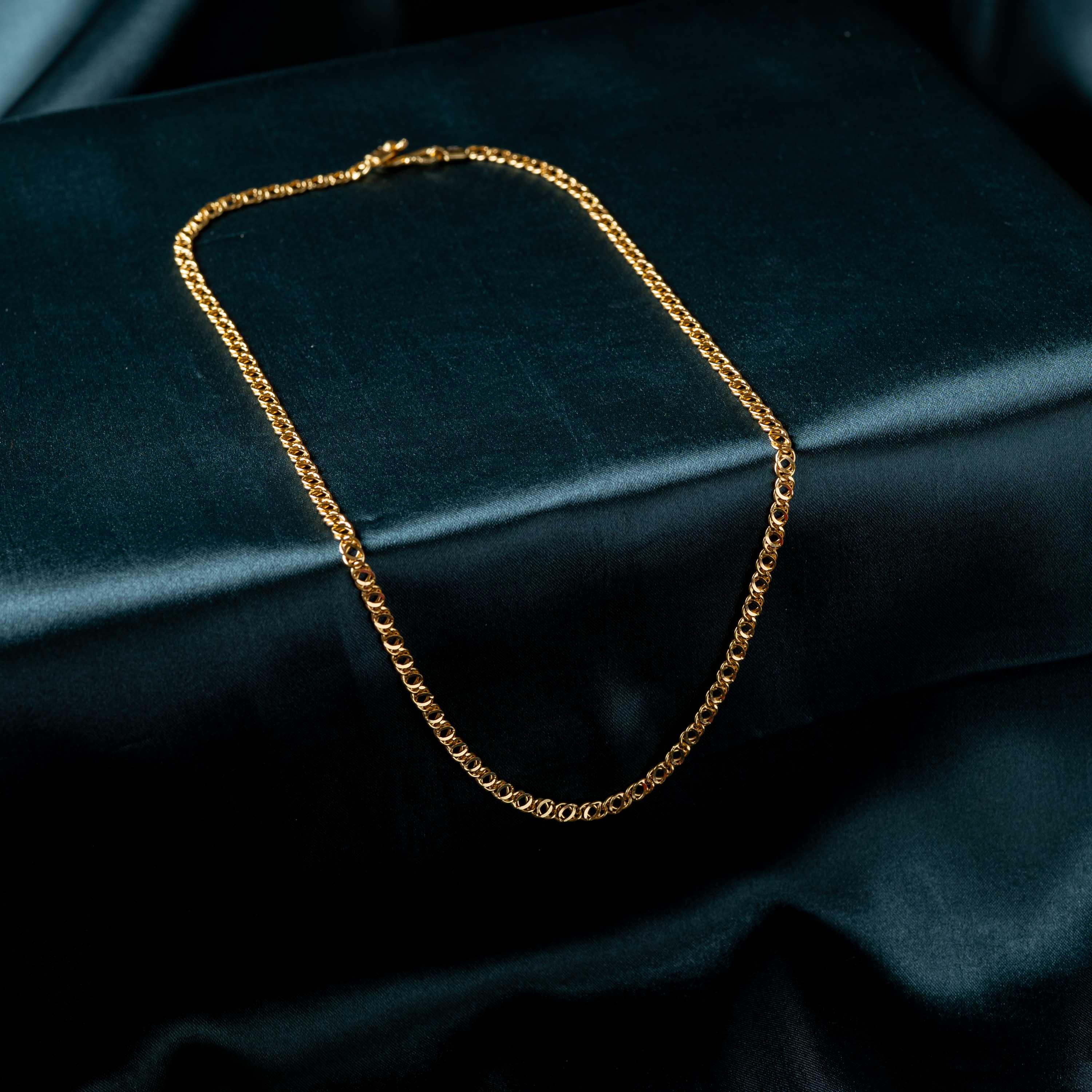 Full length of the openwork link chain laid in a loop on satin, gold plated 925 silver