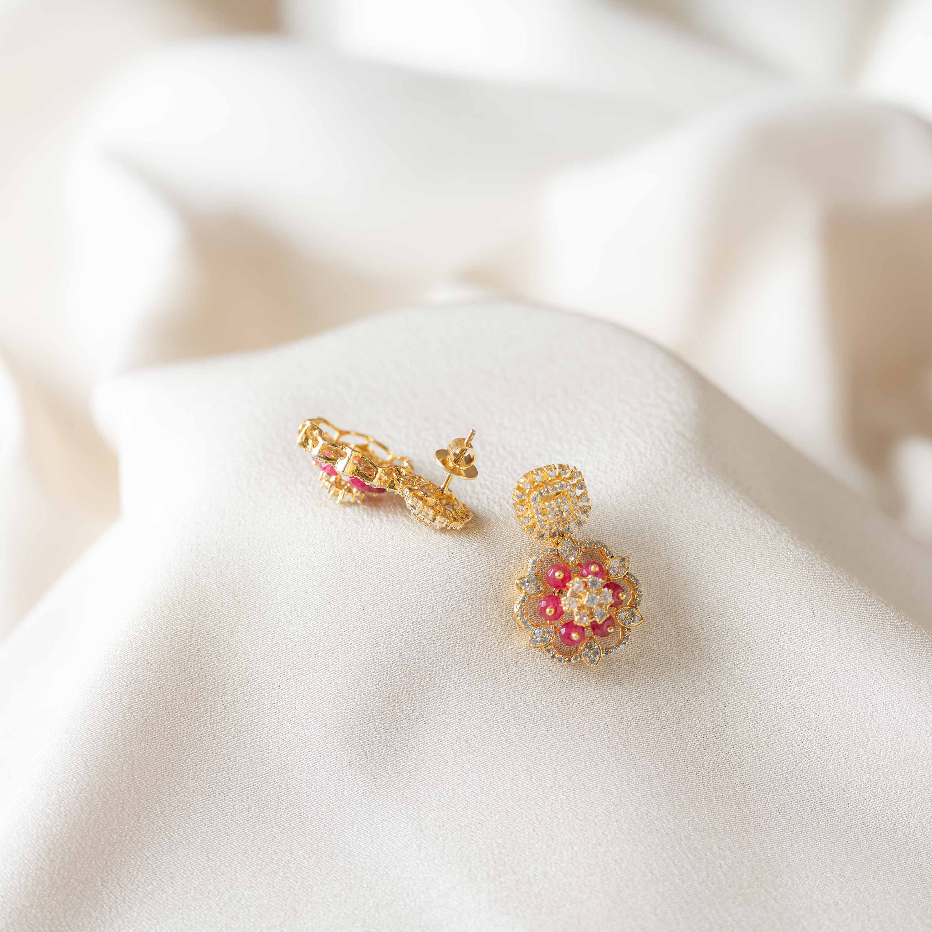 Close-up of Rosira hanging earrings crafted in 925 sterling silver with gold plating, floral CZ design and red crystal beads