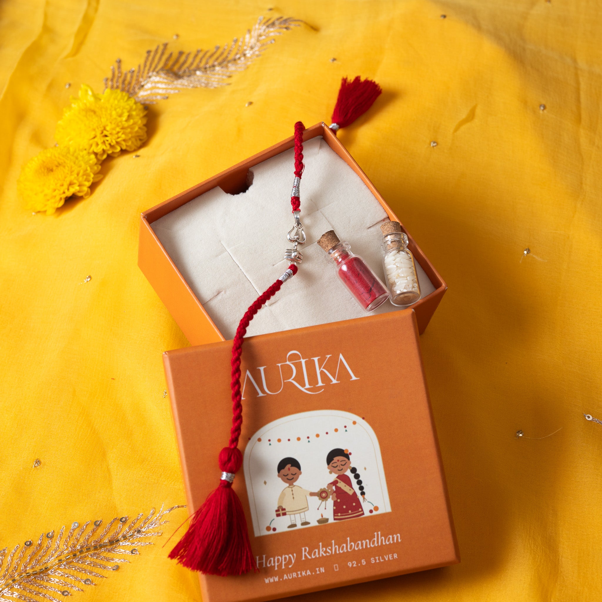 Trishul and shivling rakhi with its red cord in an open Aurika gift box with roli and akshat vials